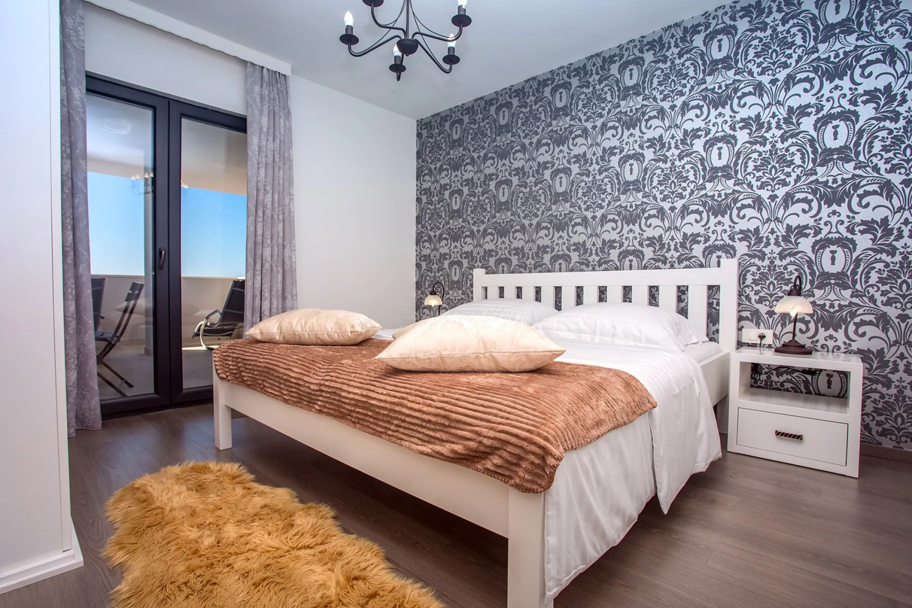 A bedroom with a white bed against a patterned accent wall.