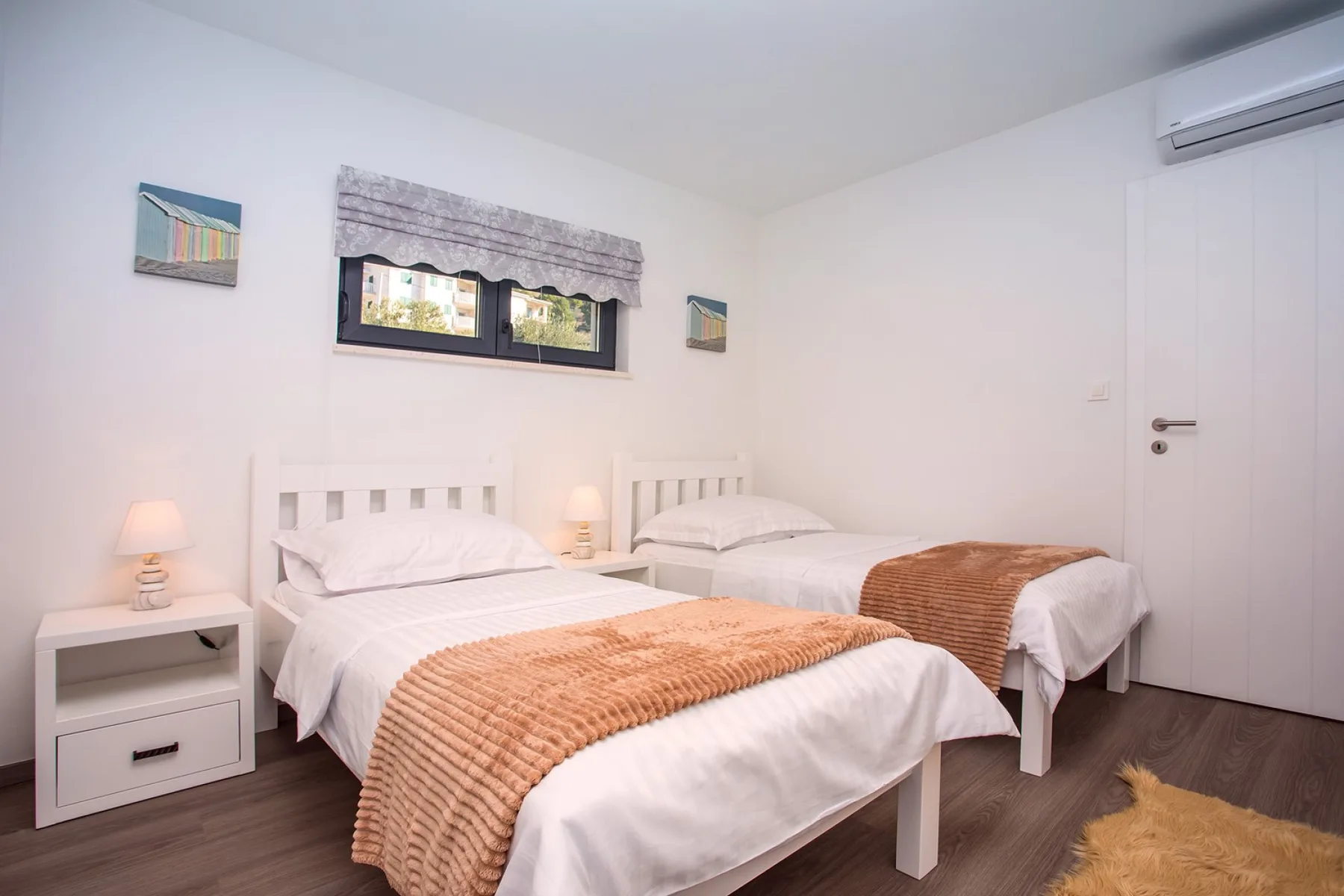 A bright bedroom with two beds, white bedding, and a small window.