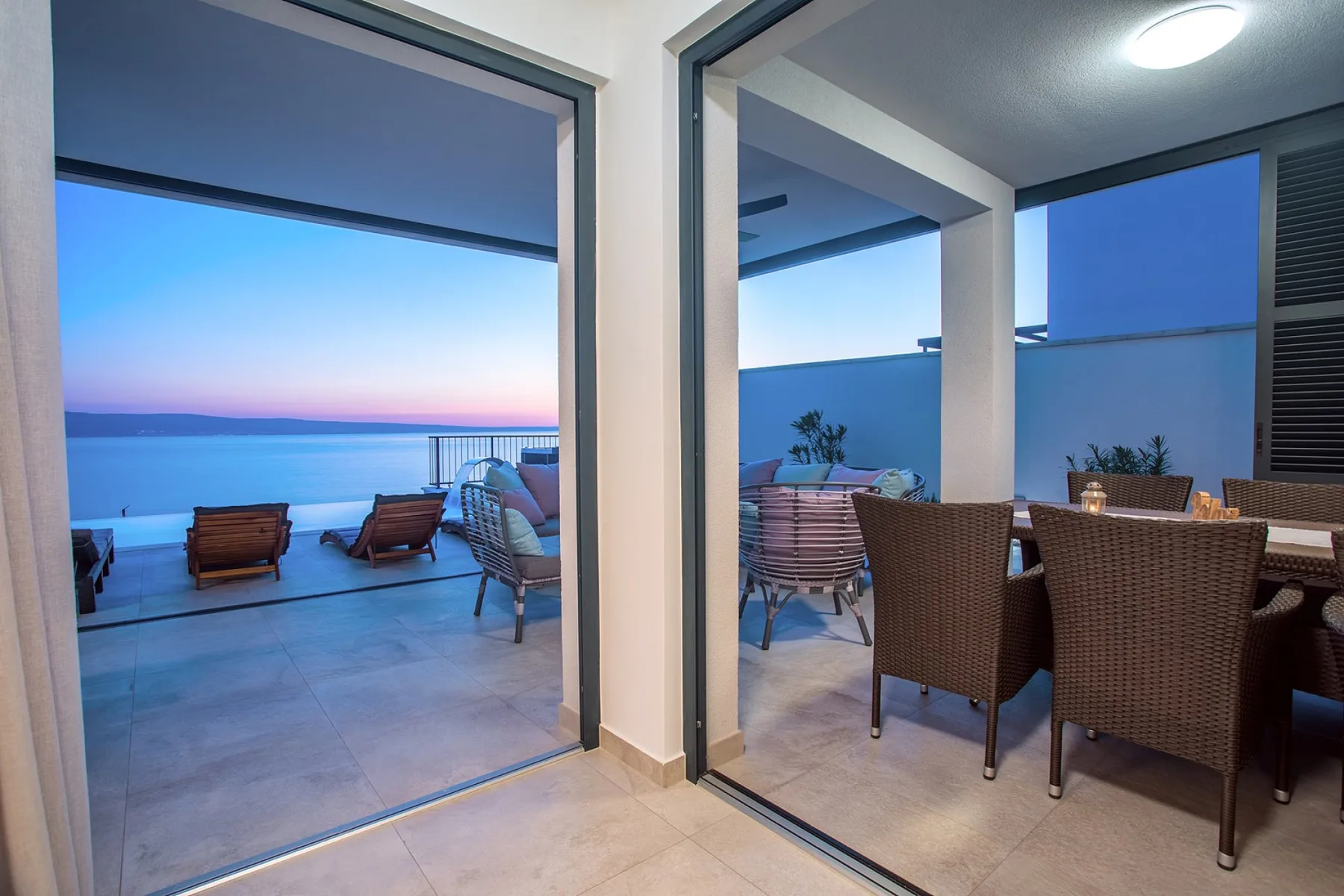 A covered patio with dining seating overlooks the water at dusk.