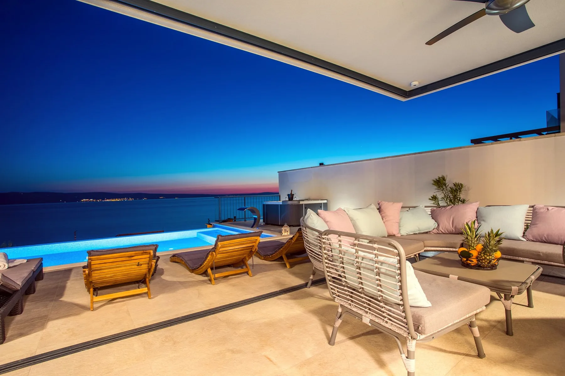 A rooftop terrace overlooks the ocean at dusk, with a pool and outdoor seating.