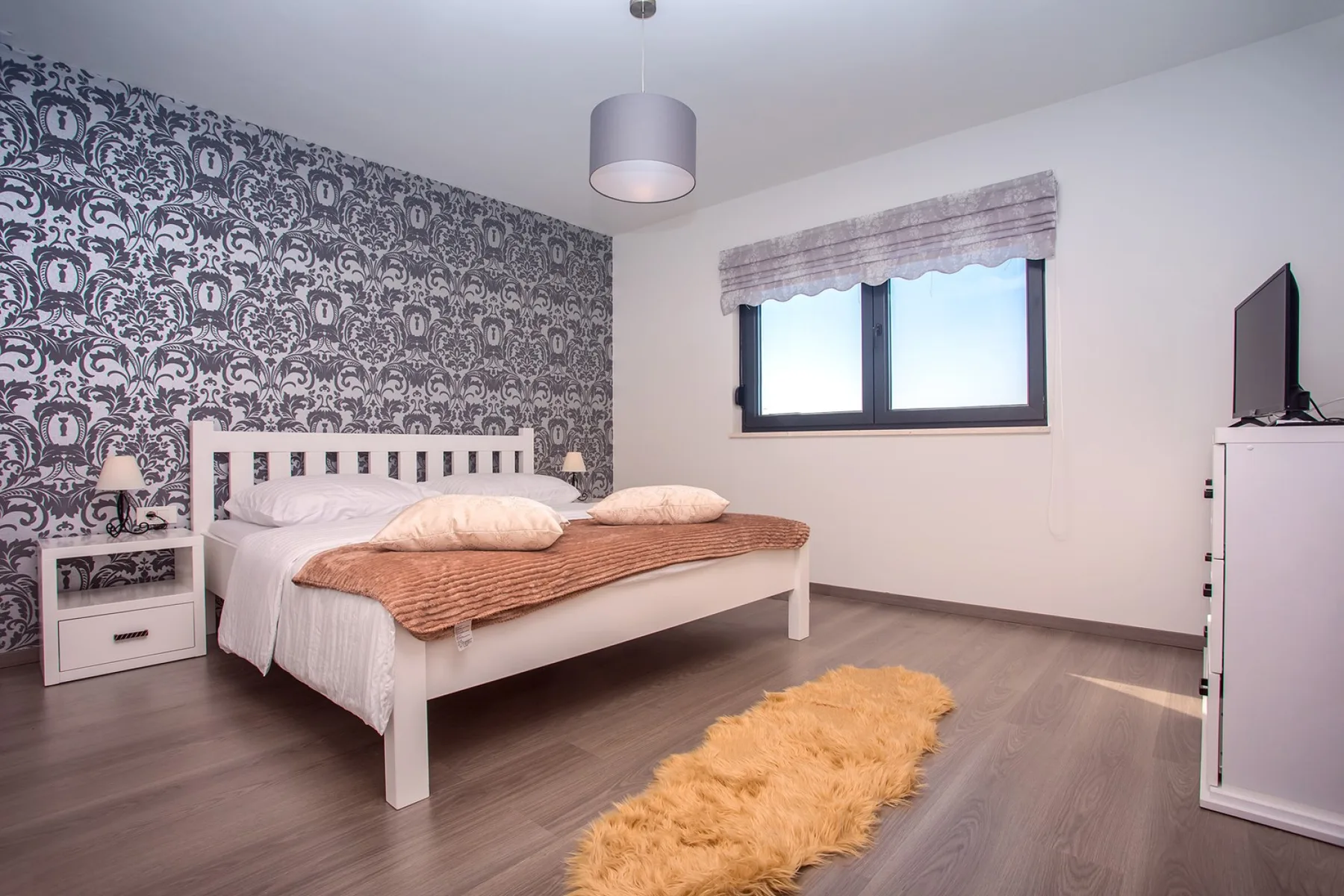 A bedroom with a bed, patterned accent wall, and window.