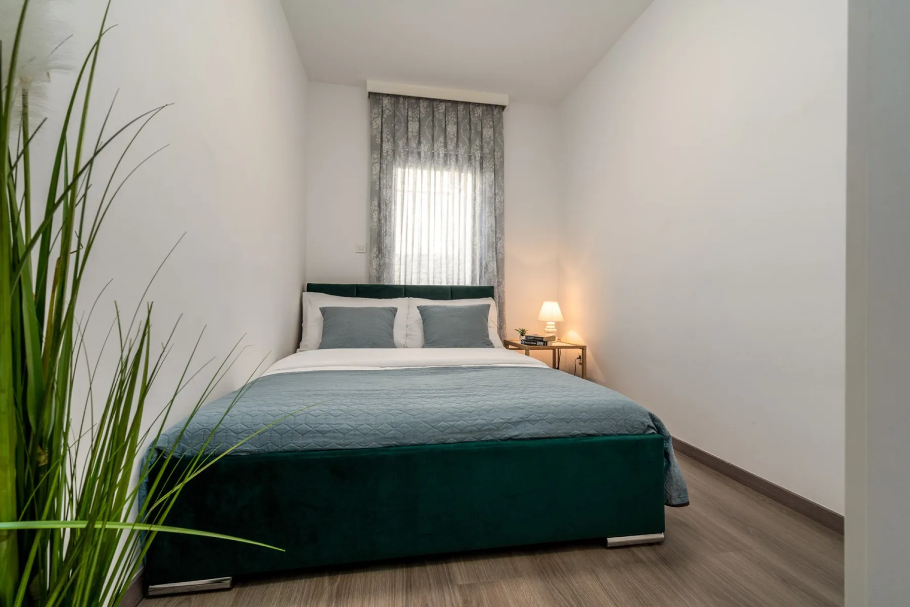 A bedroom with a neatly made bed beneath a curtained window.