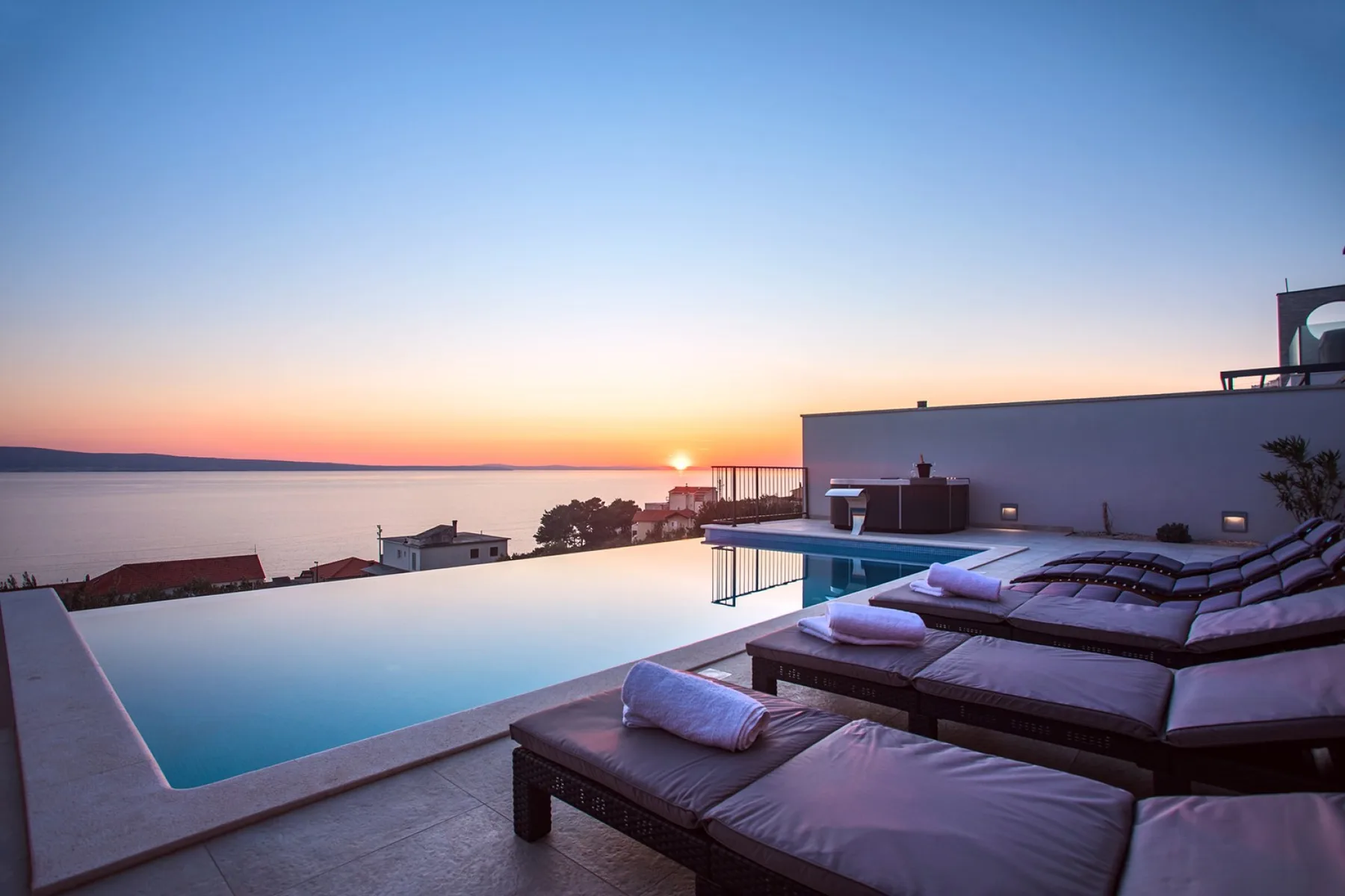 A rooftop pool and lounge seating overlook the sea at sunset.