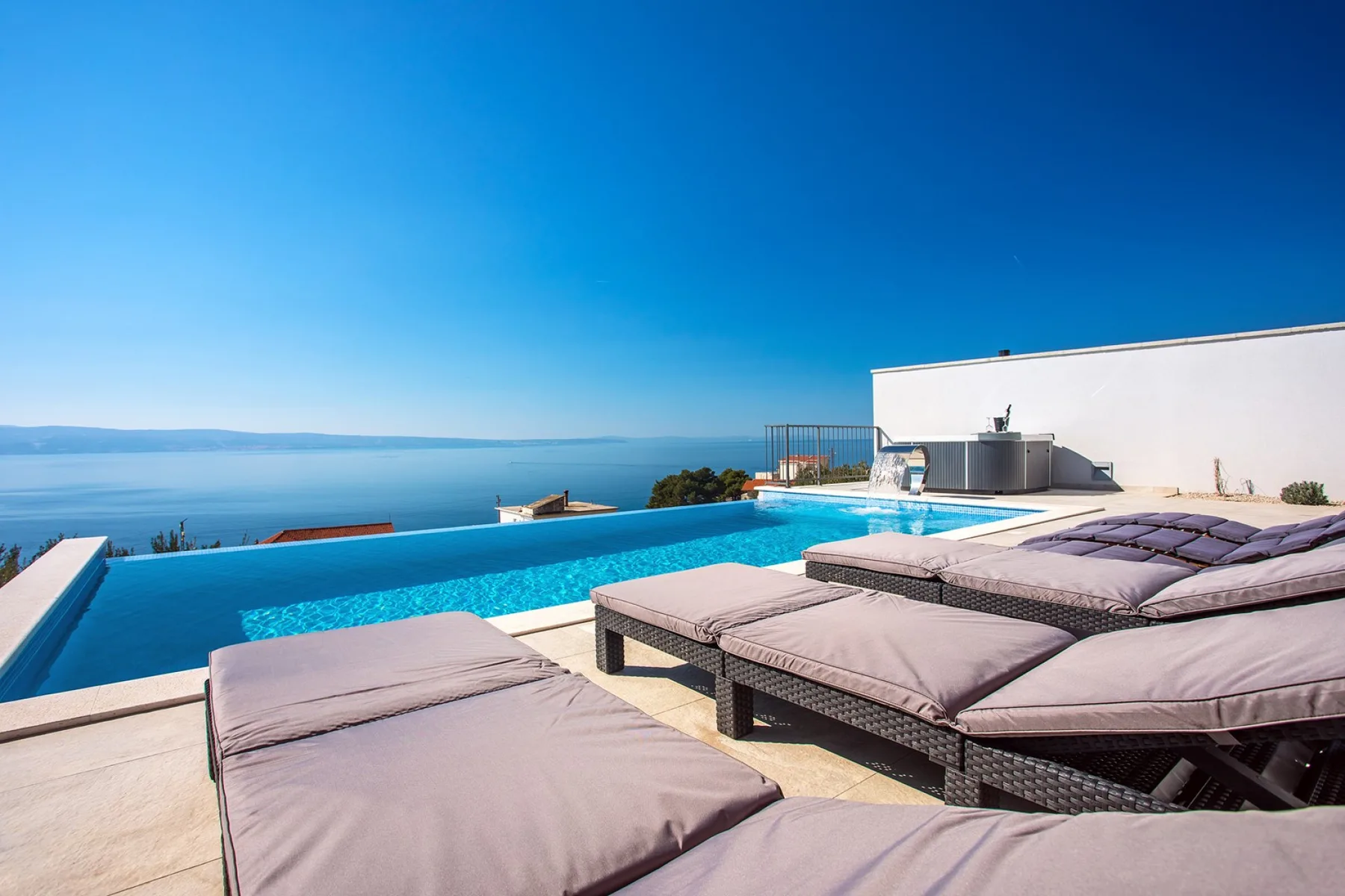 An outdoor pool overlooks the water, with cushioned lounge seating on the deck.
