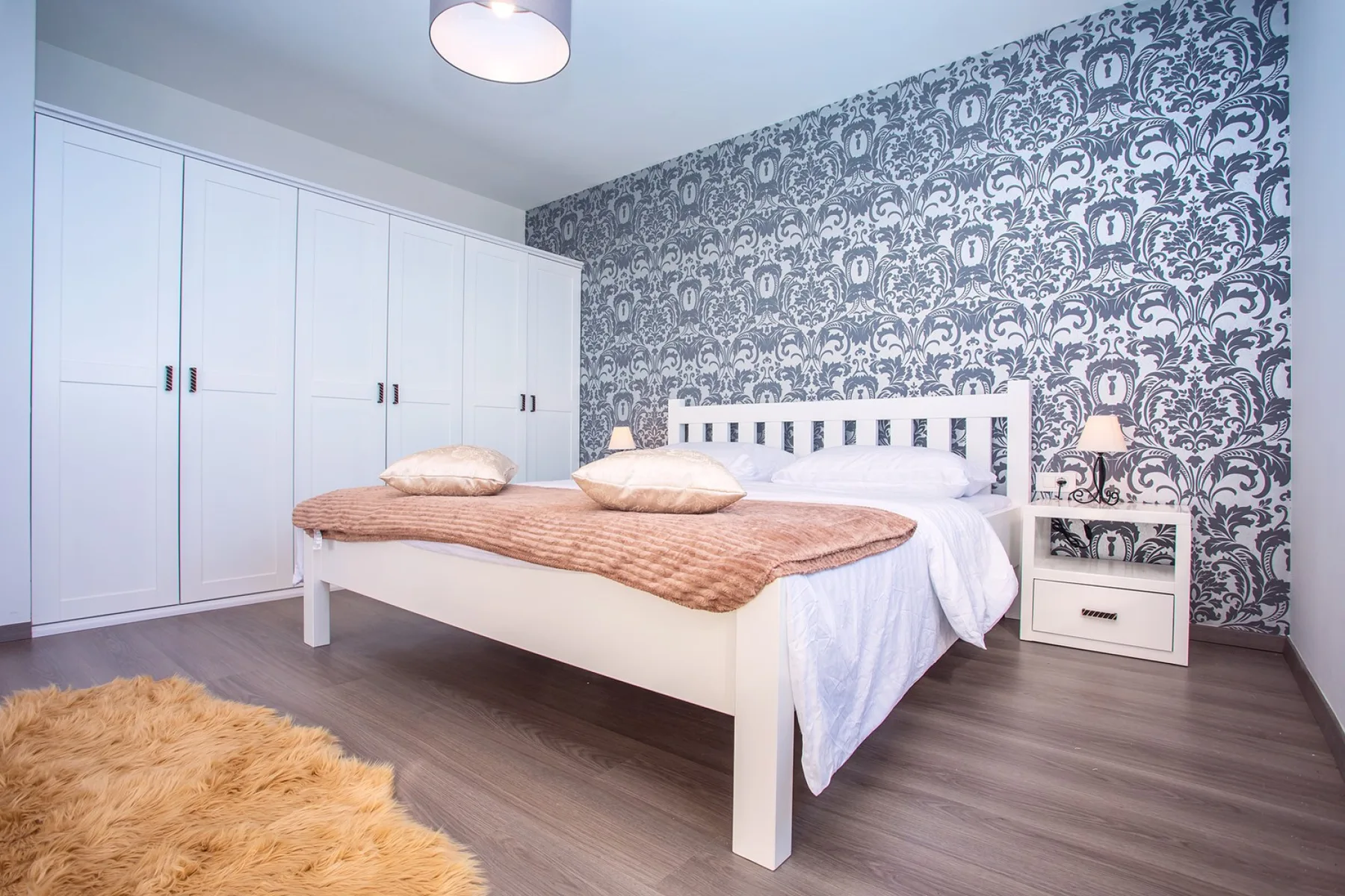 A bedroom with a white bed, patterned wallpaper, and built-in wardrobes.