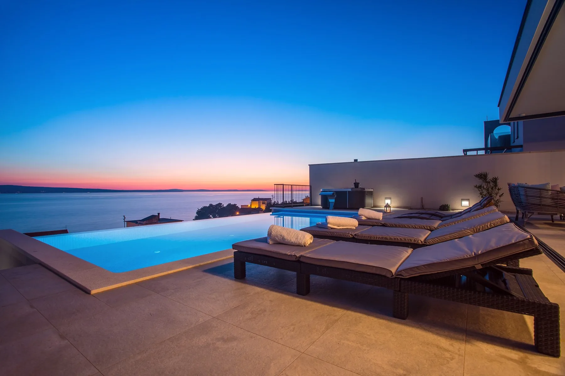 An outdoor pool overlooks the sea beside a patio with lounge seating.
