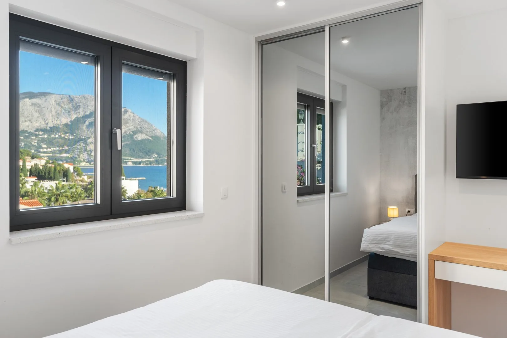 A bright bedroom with a large window overlooking the water and mountains.