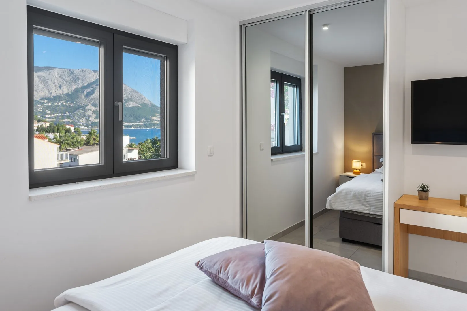 A bright bedroom with a large window overlooking the sea and mountains.