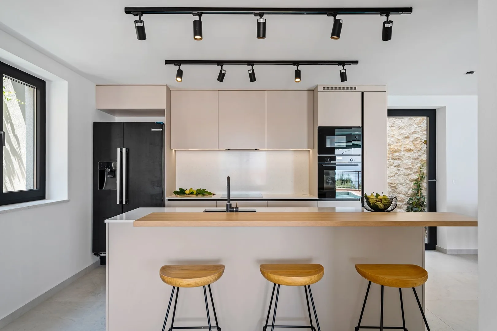 A modern kitchen with an island, bar stools, and dark appliances.