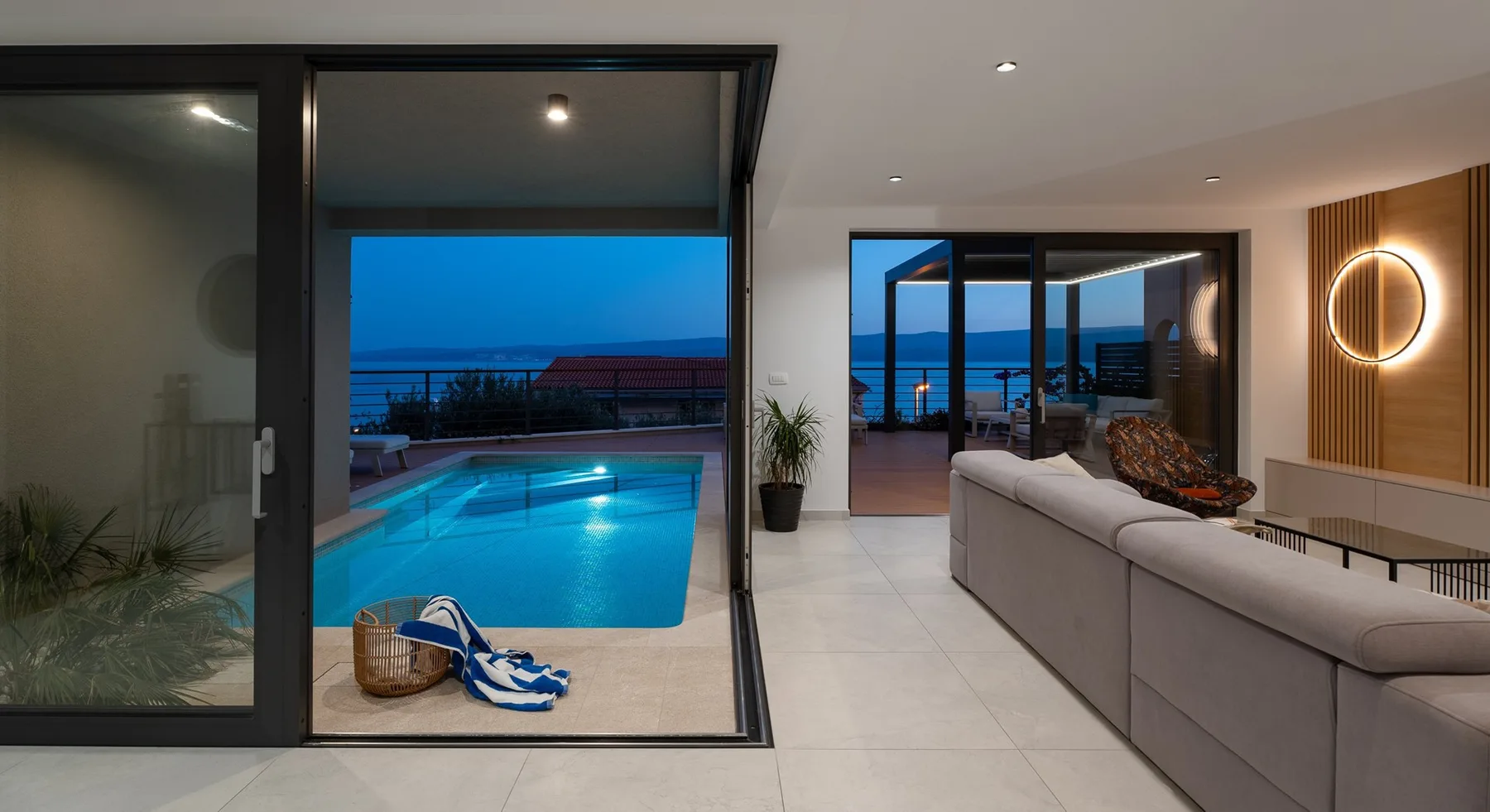 A modern living room opens onto a patio with a swimming pool and ocean view.