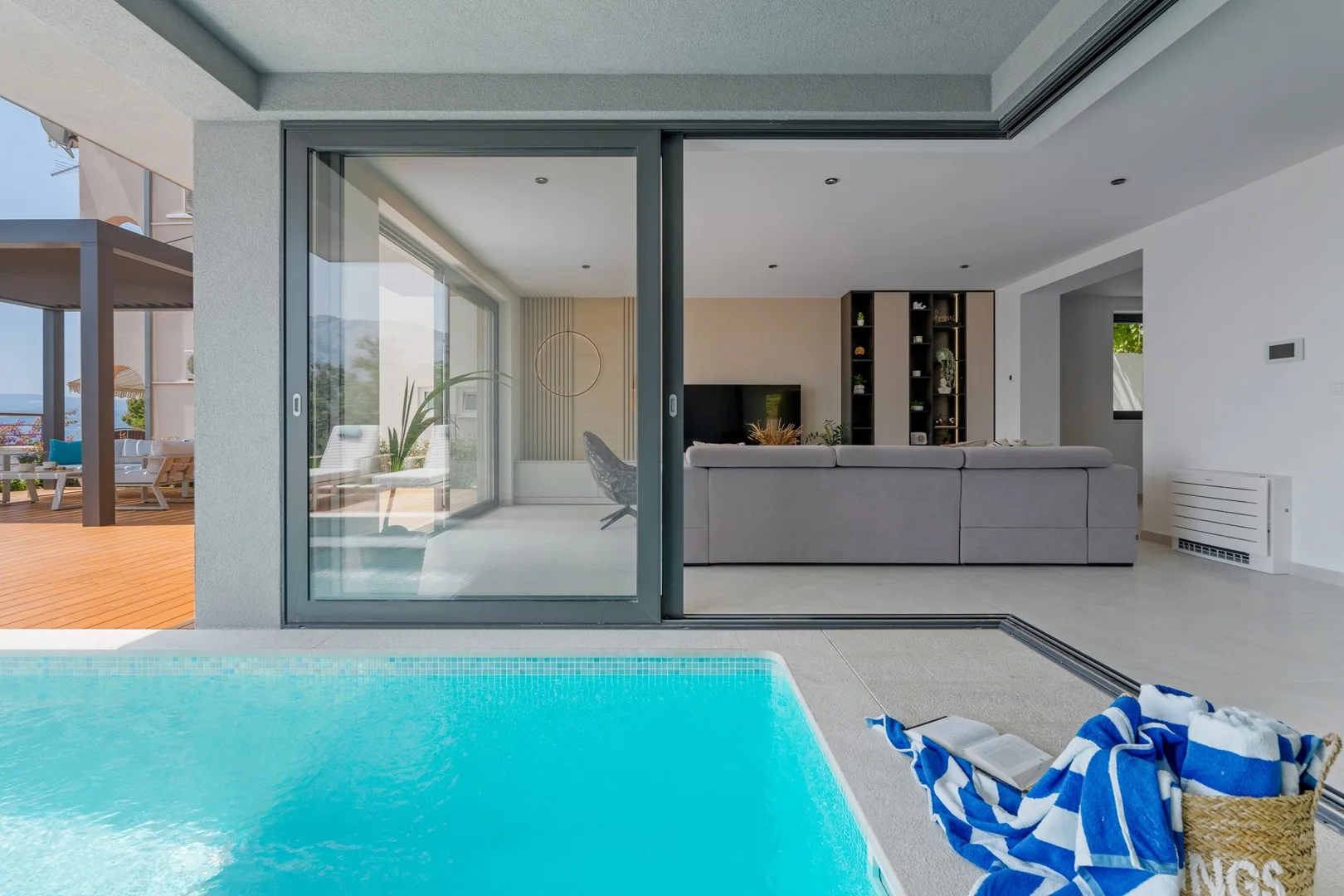 A swimming pool beside a modern living room with sliding glass doors.
