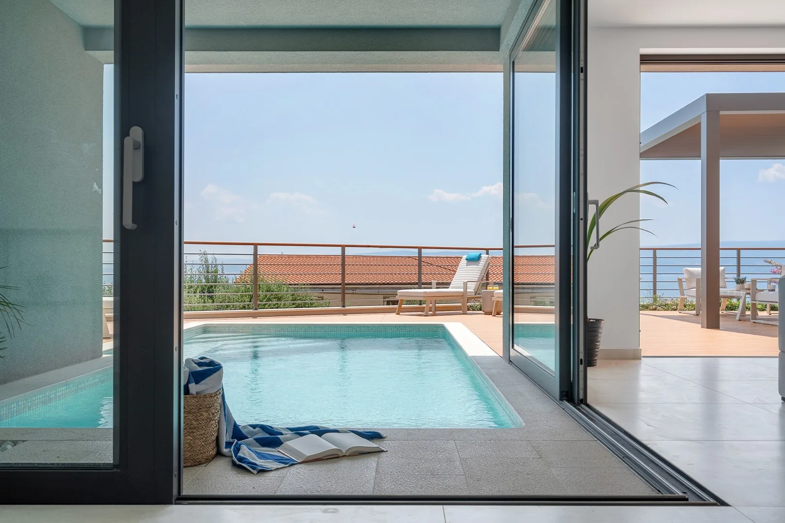 A bright indoor pool opens onto a terrace with seating and a sea view.