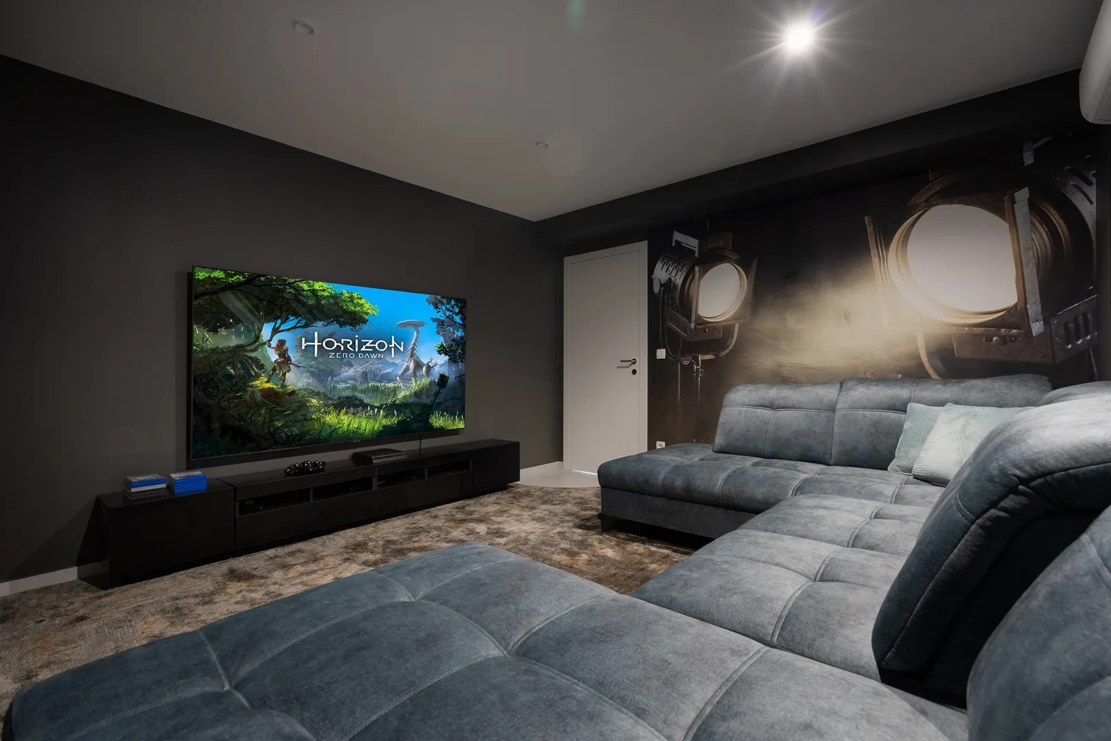 A dark living room with a large sectional sofa and television.