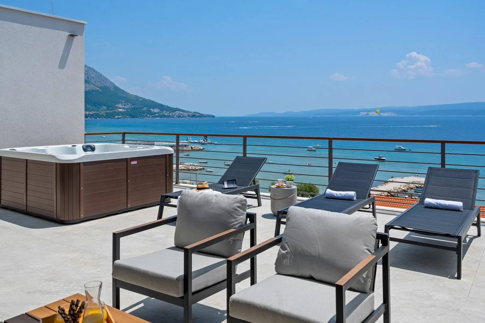 A seaside terrace with outdoor seating and a hot tub overlooking the water.