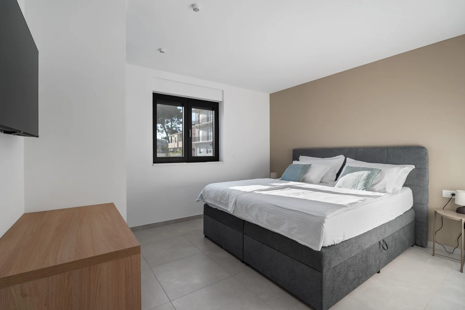 A bedroom with a neatly made bed beside a window.