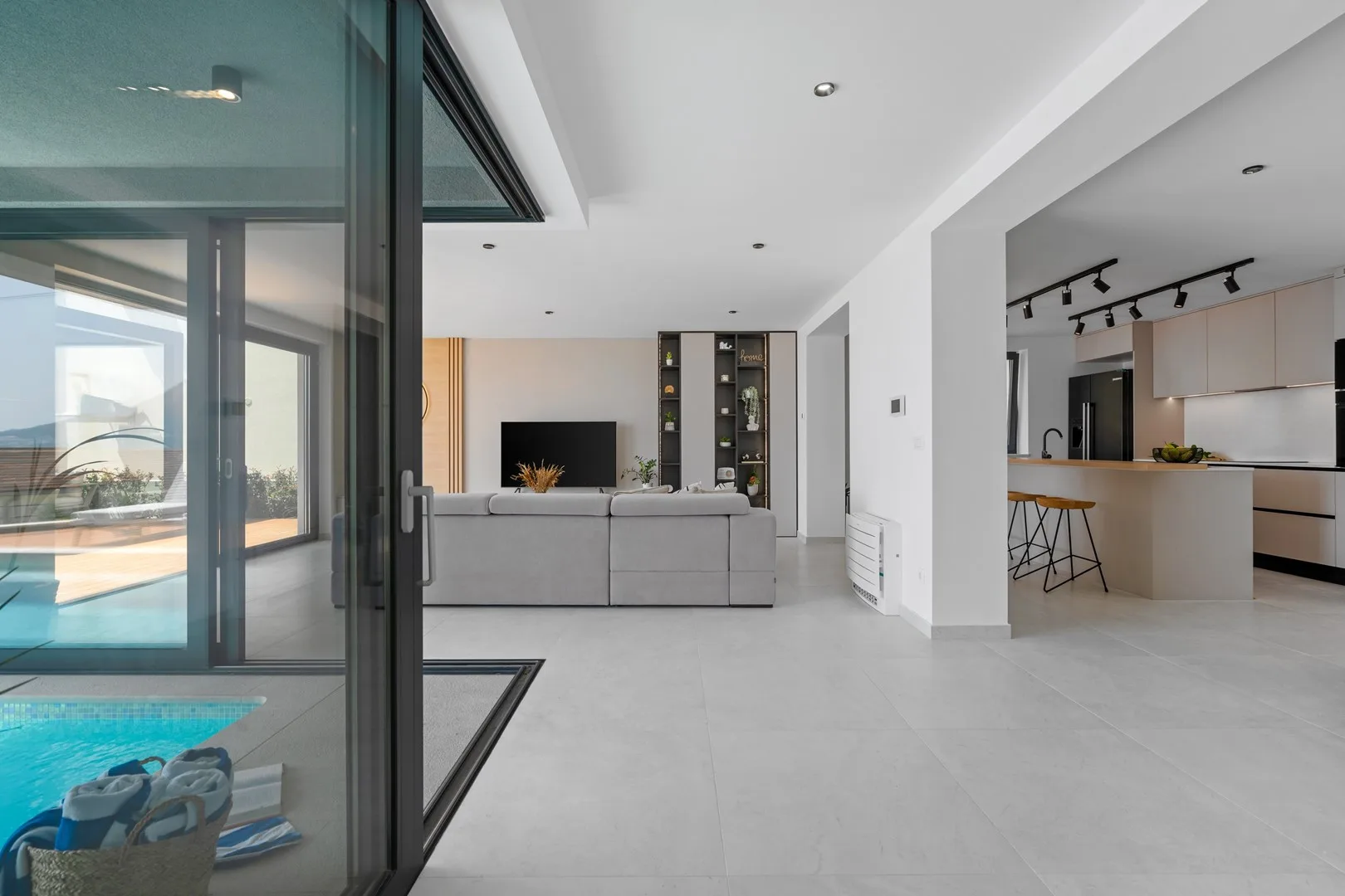 An open living area connects to a kitchen, with glass doors beside a pool.