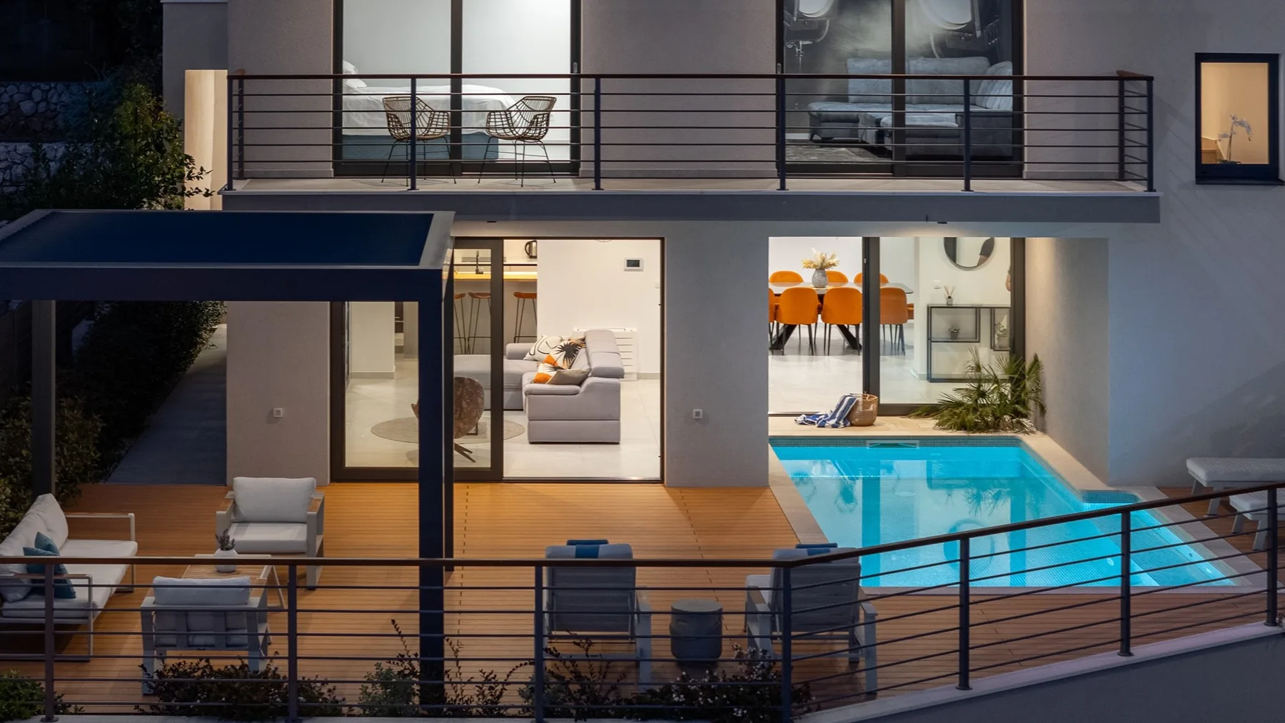 A modern house opens onto a patio with seating and a swimming pool.