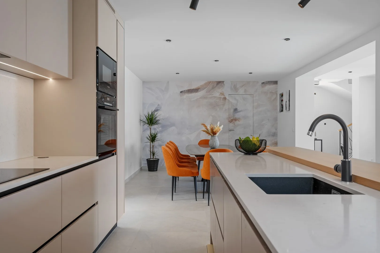 A modern kitchen with a long island, sink, and orange dining chairs.