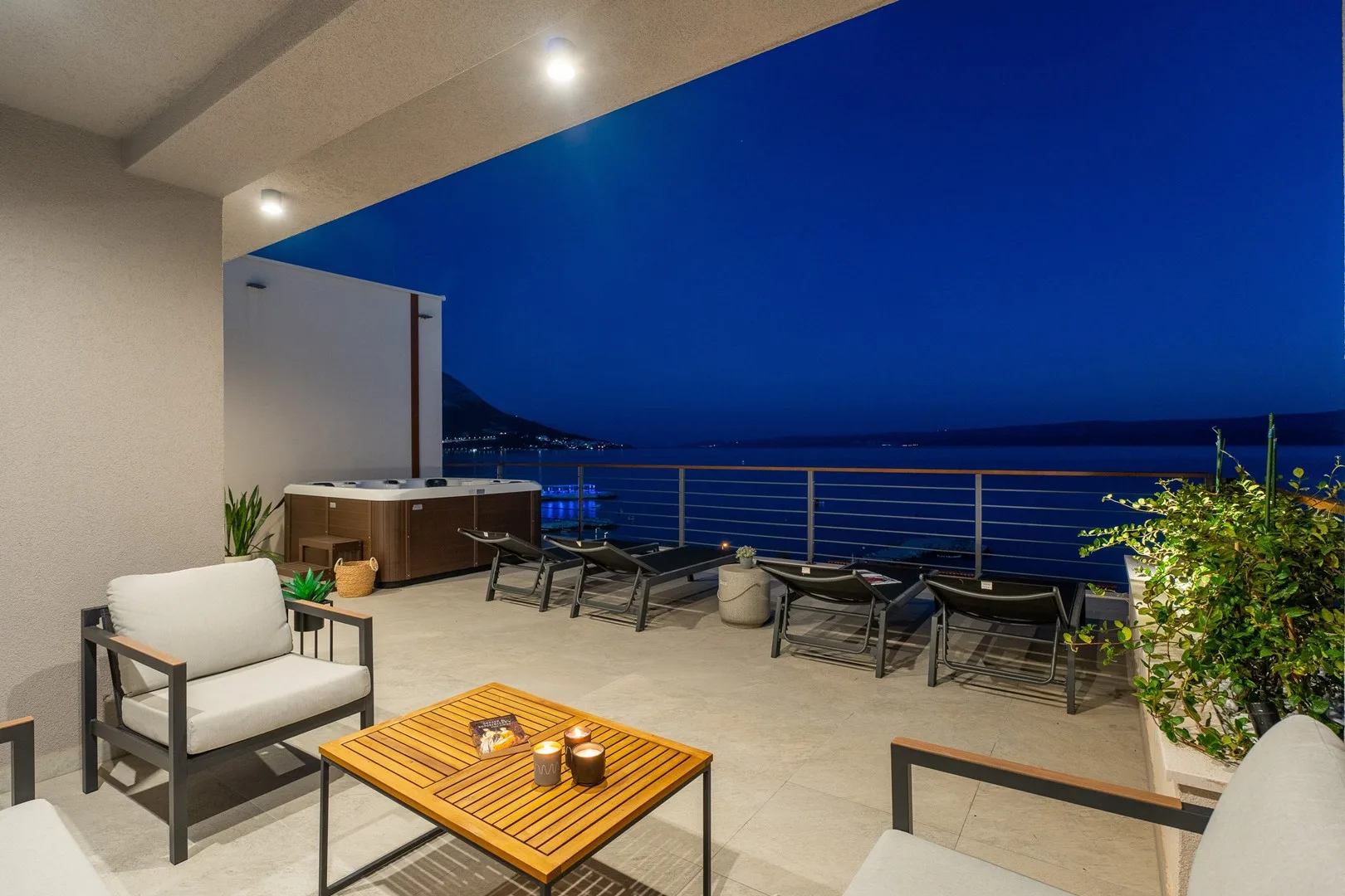 A covered outdoor terrace with seating and a table overlooks the water at night.