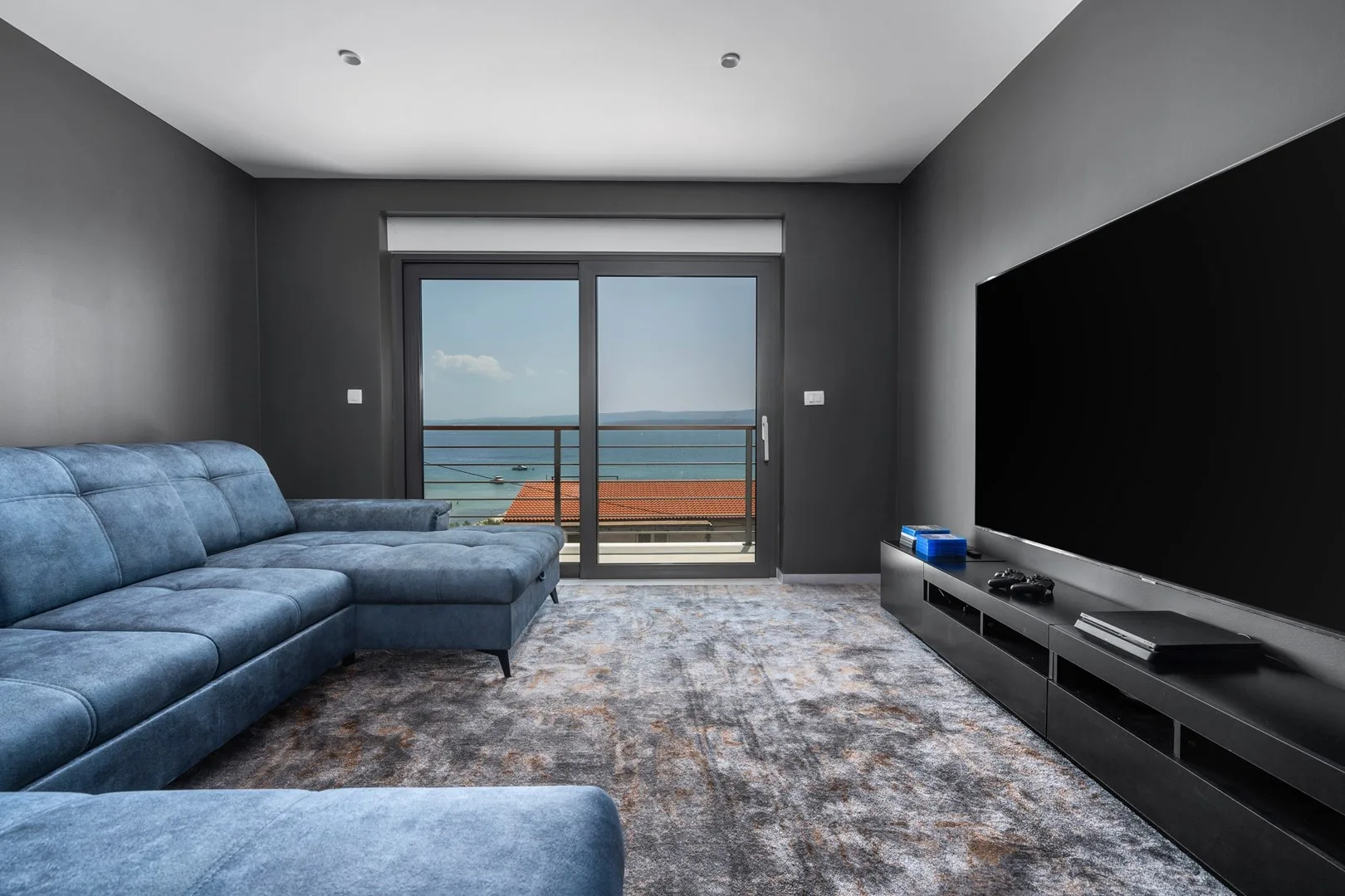 A living room with blue seating, a large television, and ocean views through glass doors.