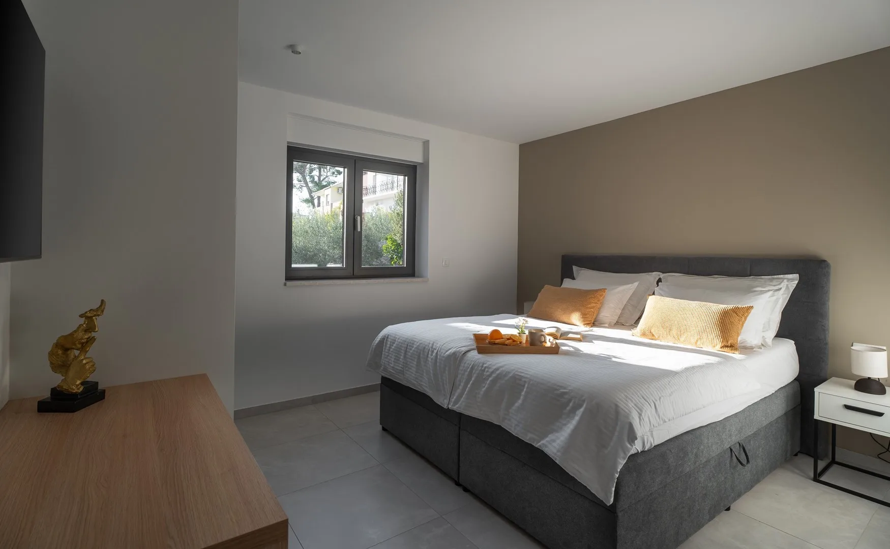 A bedroom with a neatly made bed, decorative pillows, and a window.