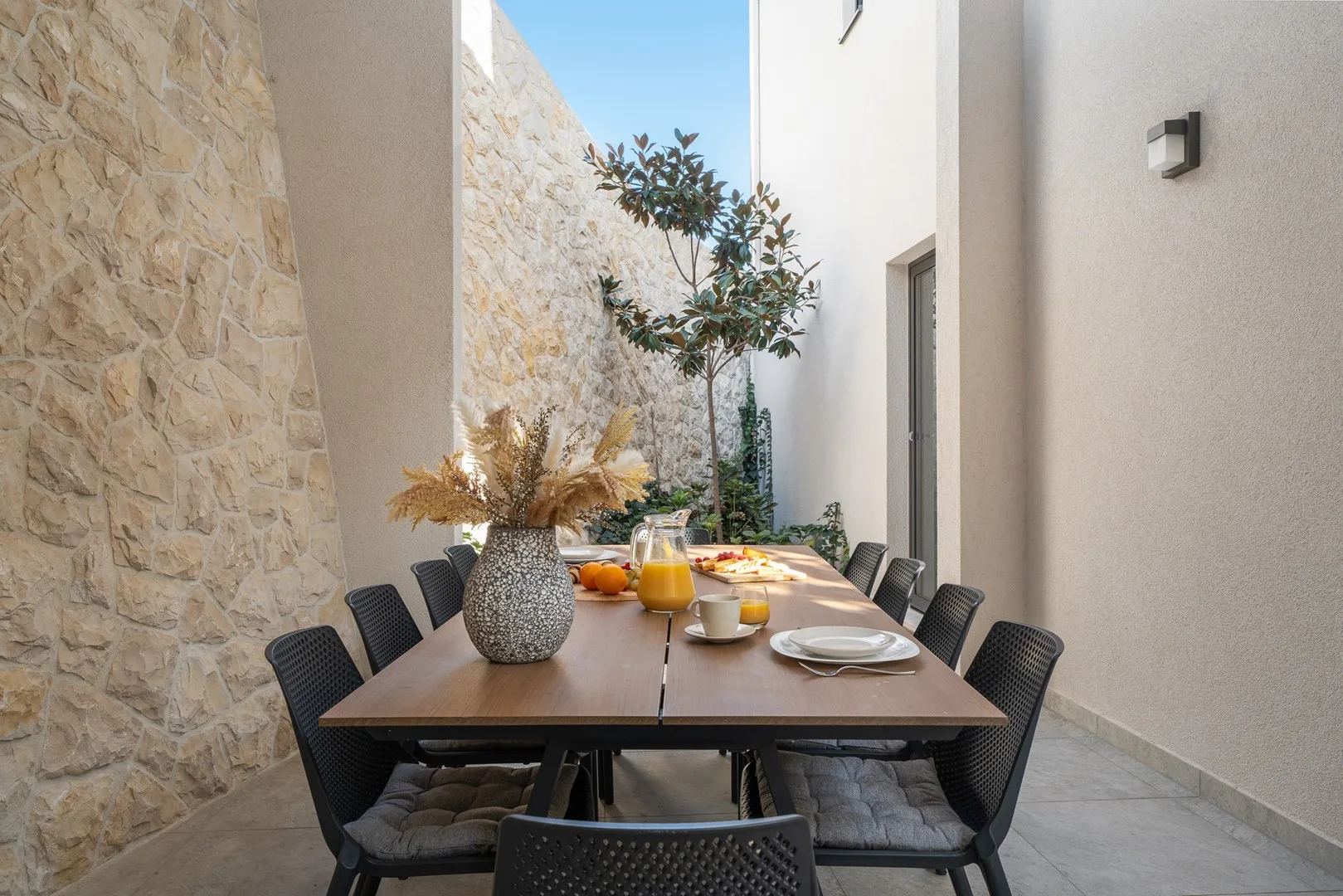 An outdoor dining table is set with dishes and drinks beside a stone wall.