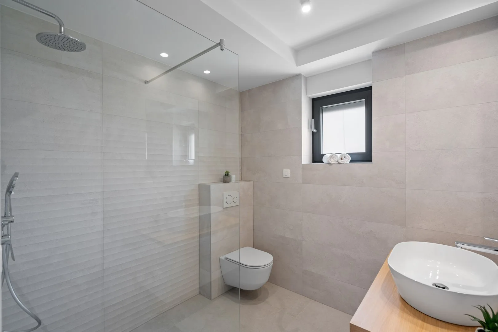 A modern bathroom with a glass shower and a vessel sink beside a window.