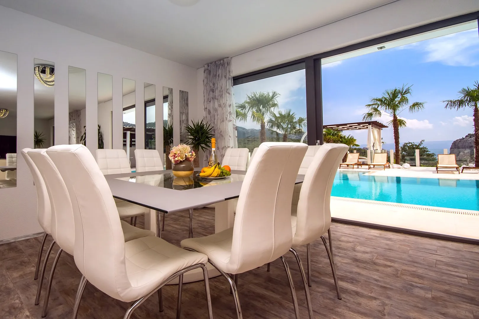 Comedor con asientos acolchados junto a grandes ventanales con vistas a una piscina.