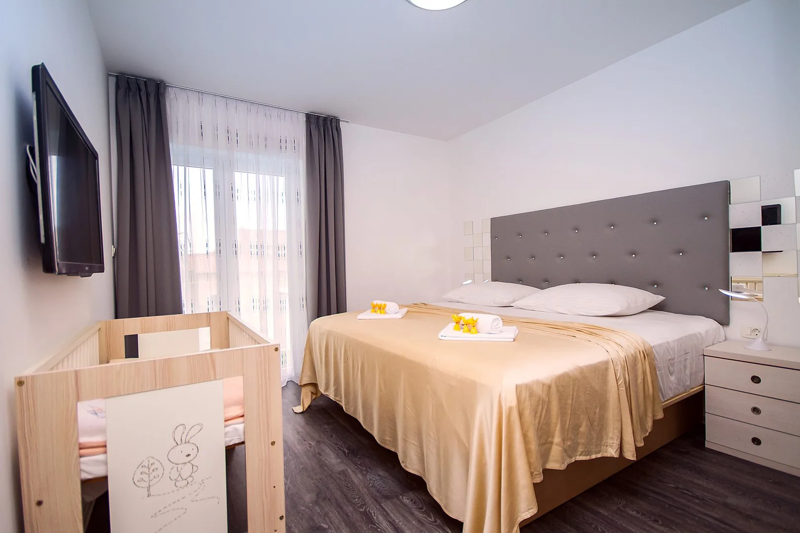 Un dormitorio con una cama grande junto a una ventana y una cuna de madera.