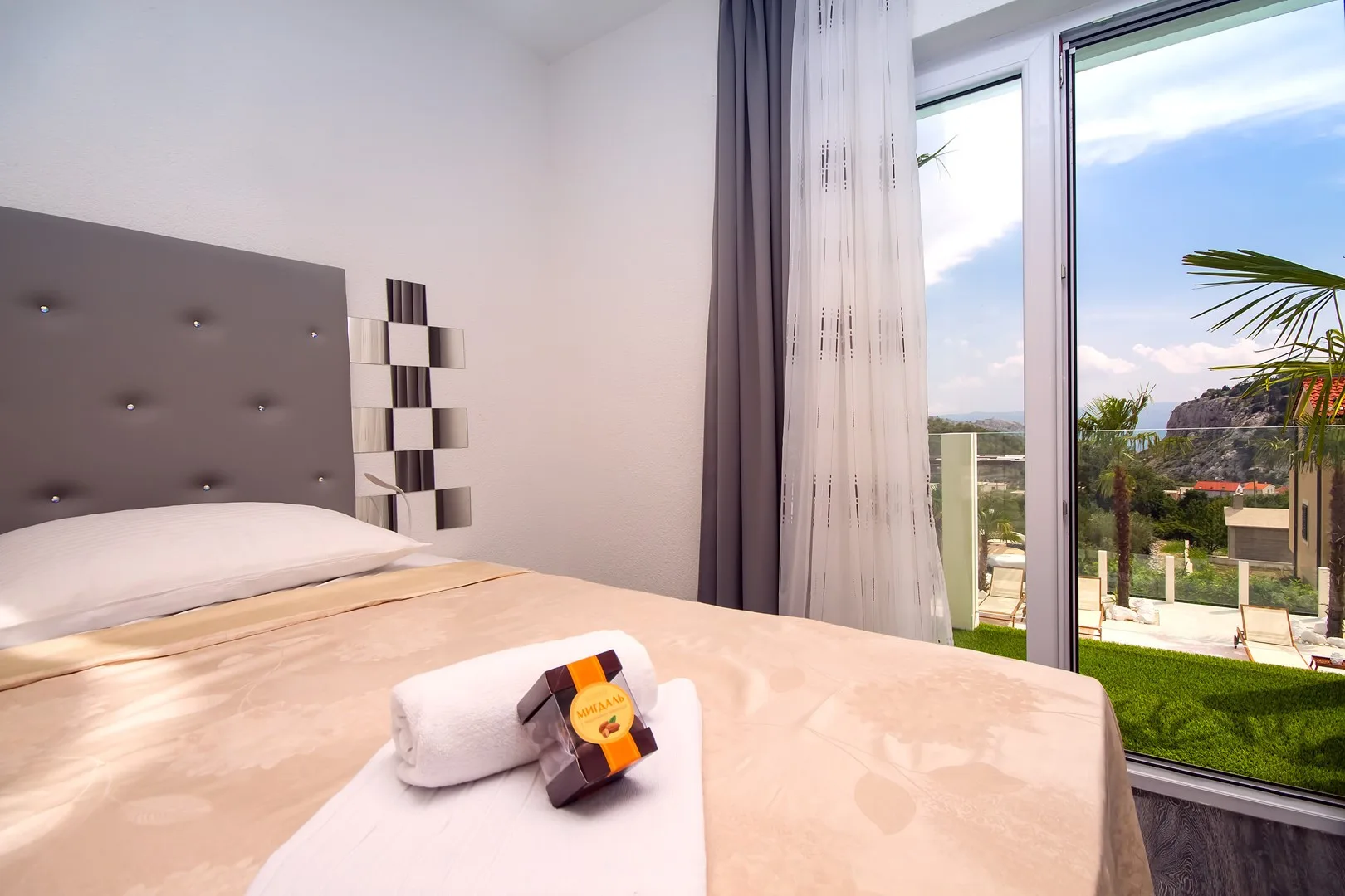 Un dormitorio luminoso con una cama tendida junto a grandes ventanas.