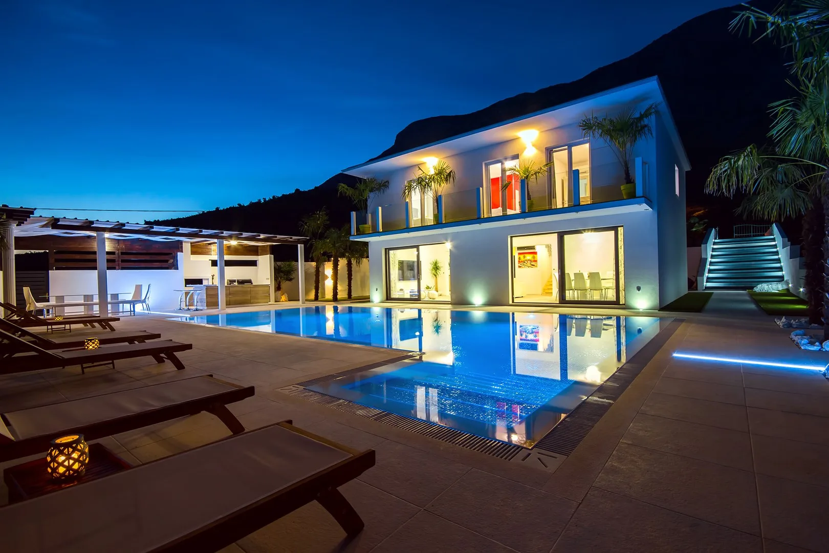 Una casa moderna da a una piscina iluminada y una zona de asientos al aire libre por la noche.