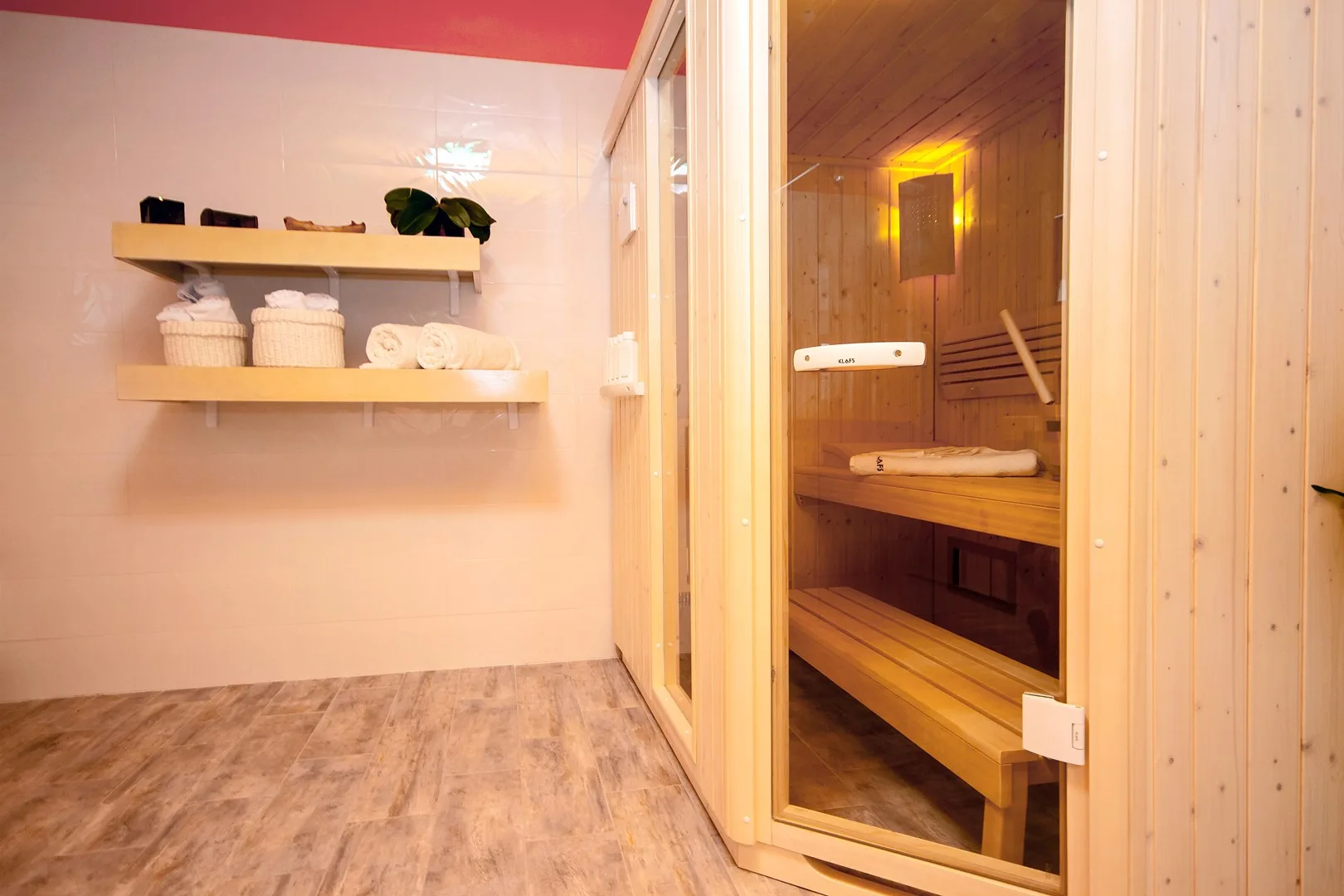 Una sauna de madera junto a una habitación con azulejos y estantes con toallas.