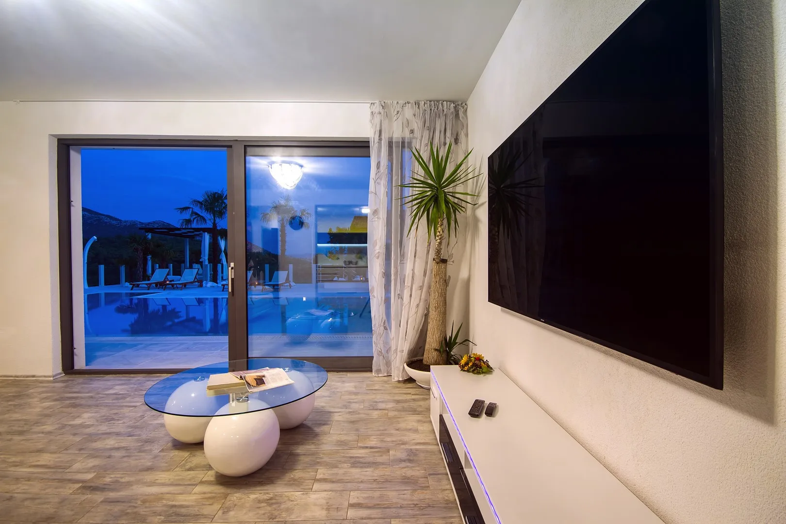 Una sala de estar con un televisor grande y una puerta de vidrio con vista a una piscina.