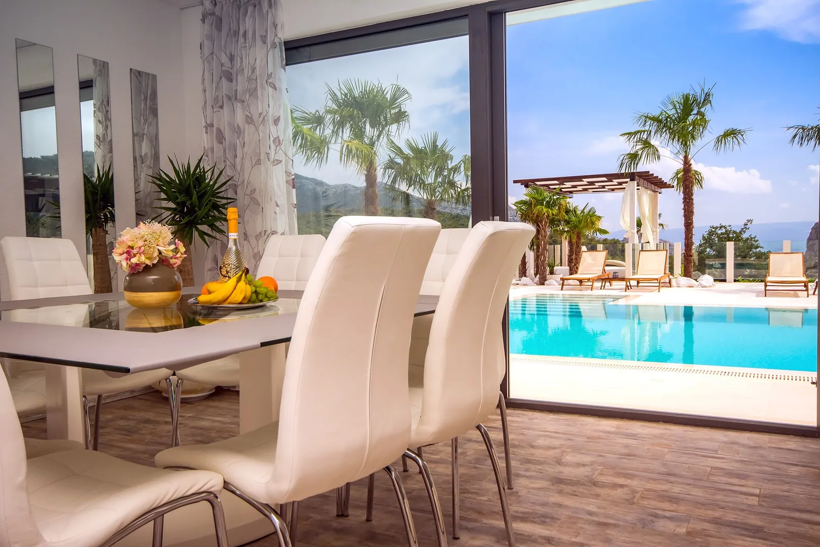 Un comedor con mesa y asientos tiene vistas a una piscina exterior.