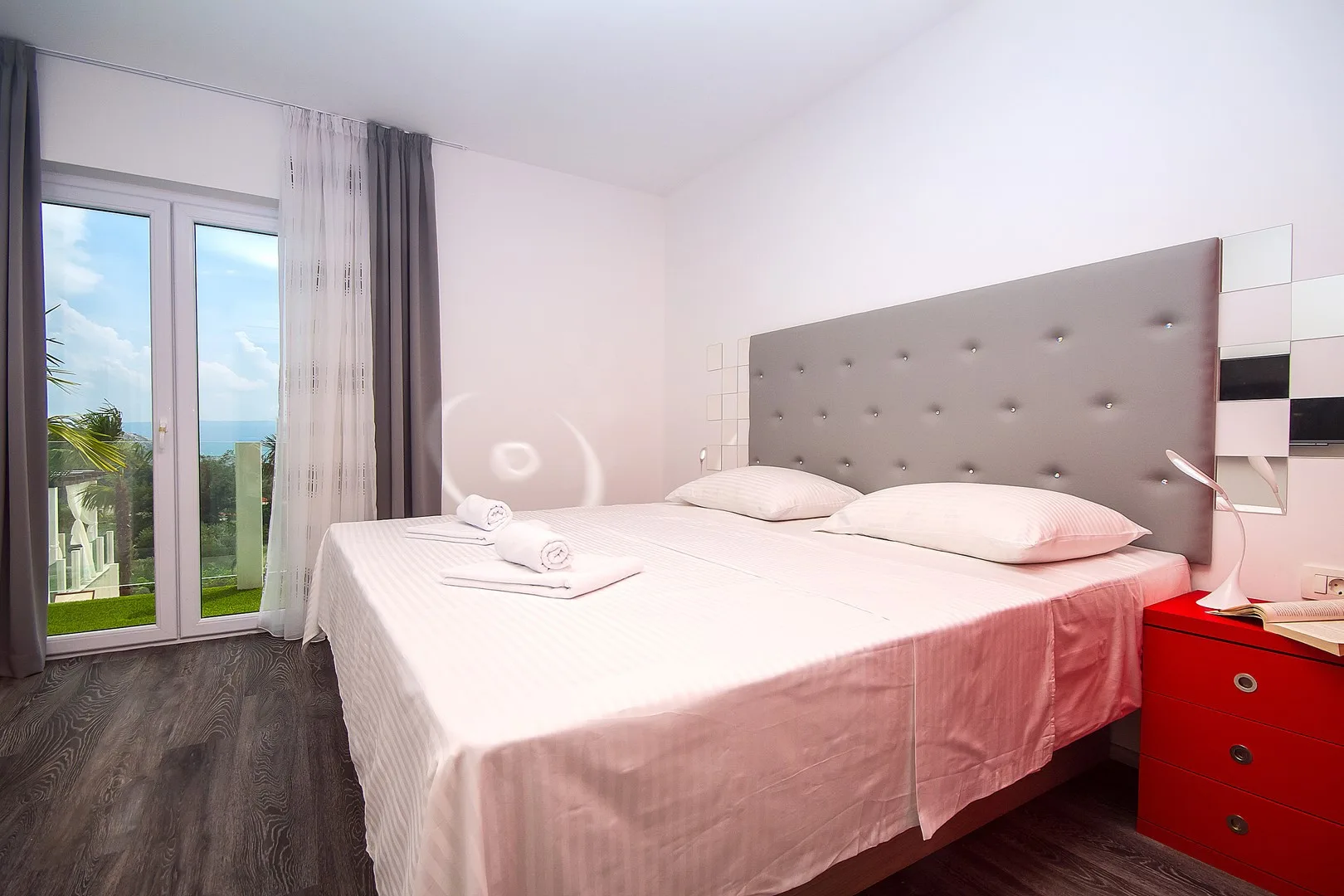 Un dormitorio con una cama, ropa de cama rosa y puertas de vidrio que dan a un balcón.