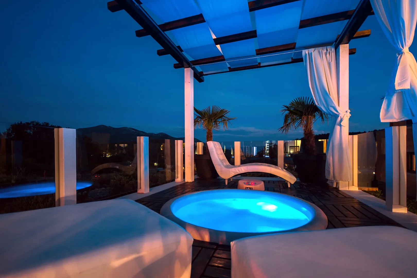 Una terraza en la azotea al anochecer tiene una piscina redonda iluminada bajo una pérgola.