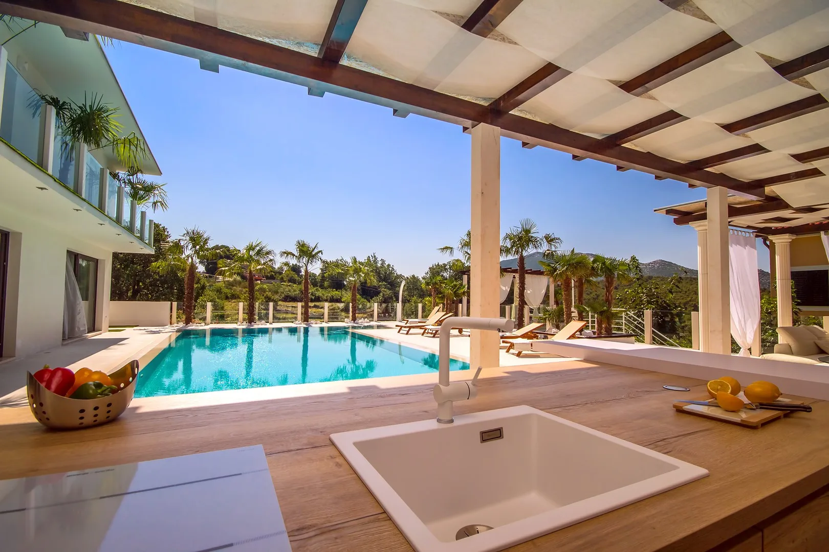 Una cocina exterior cubierta da a una piscina y palmeras.