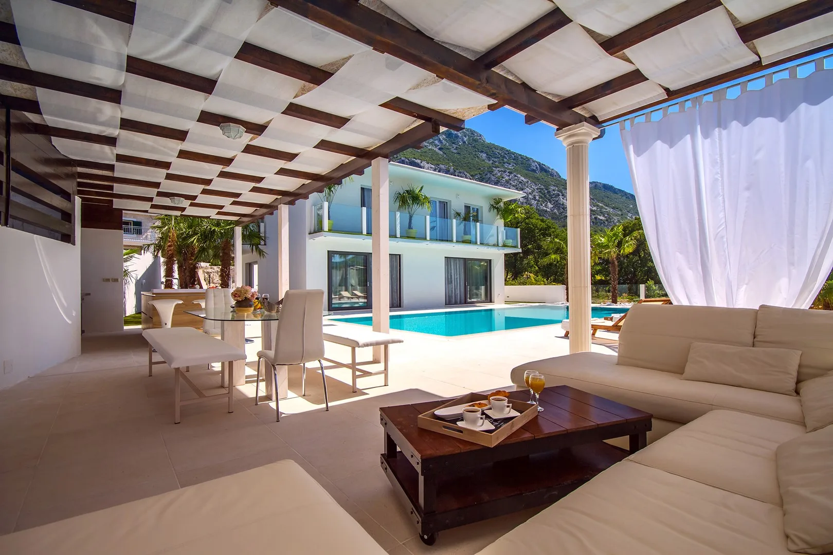 Un patio cubierto con asientos da a una piscina y una casa moderna.