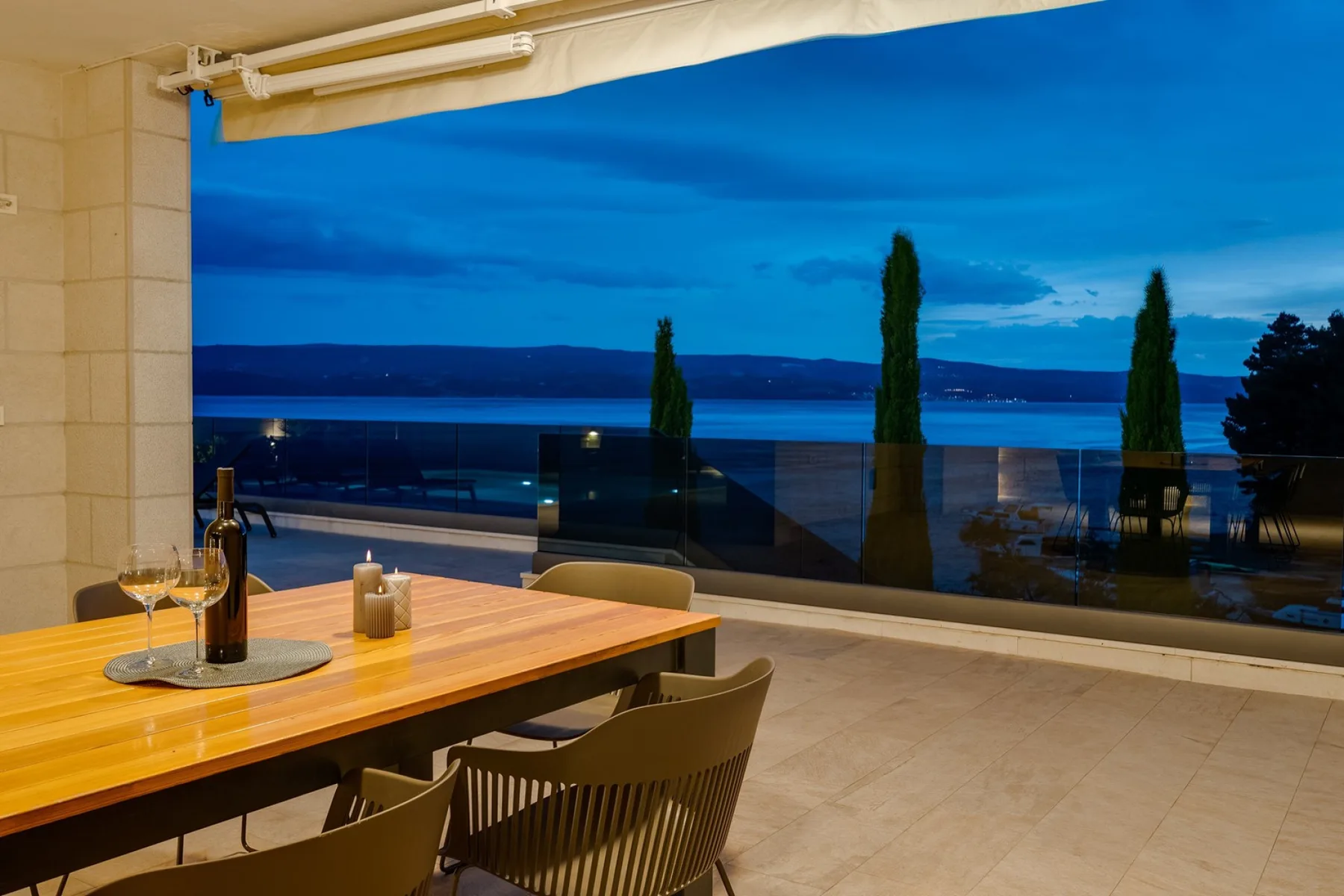 A dining area opens onto a terrace with a view of the water at dusk.