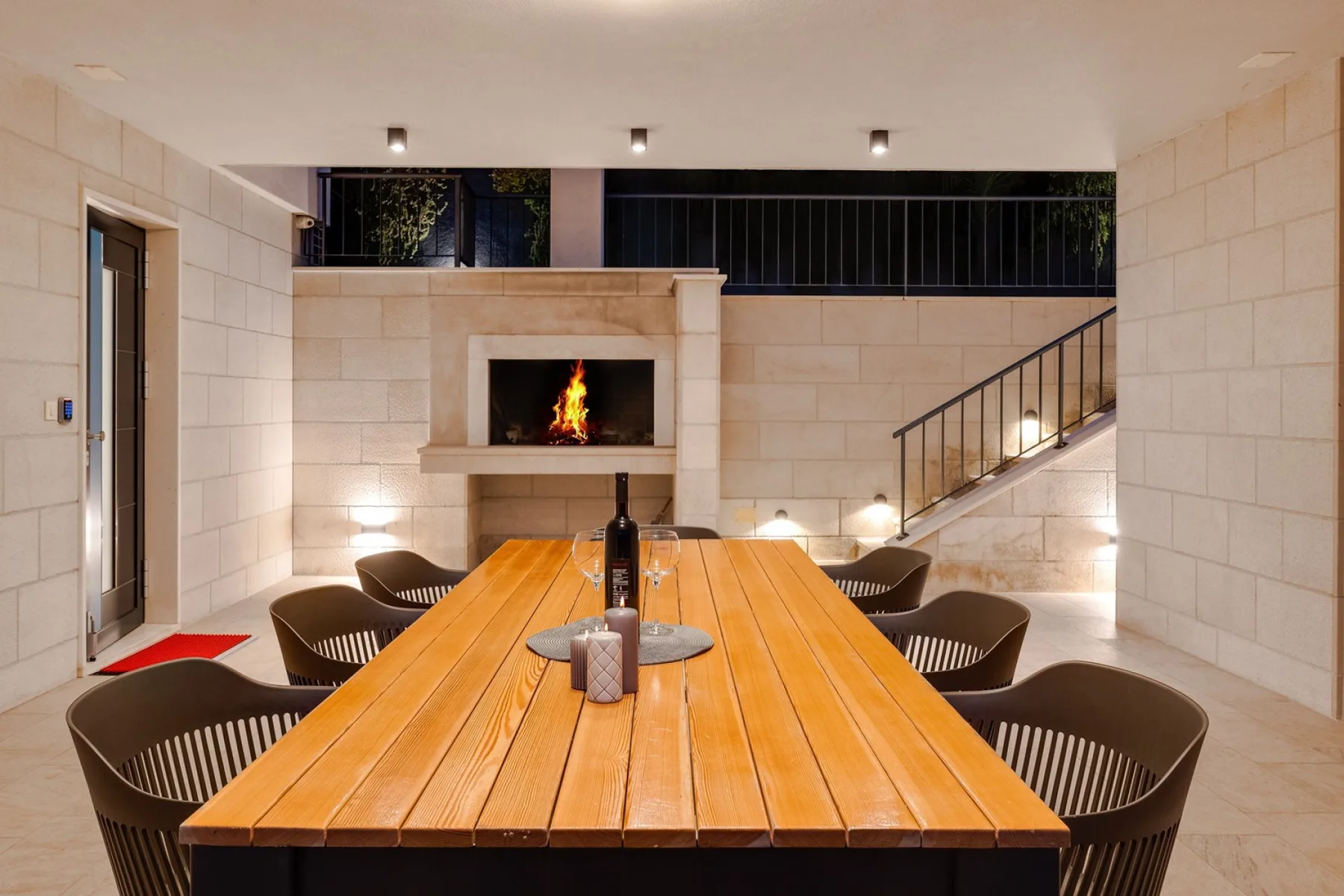 A dining area with a long wooden table and a lit fireplace.