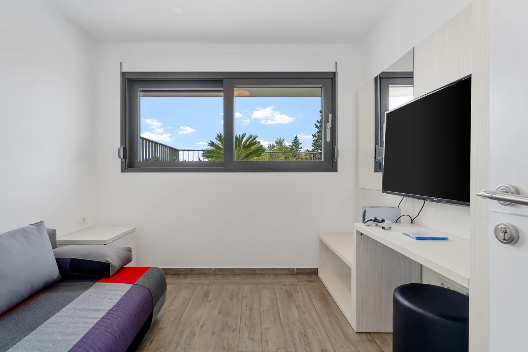 A compact bedroom with a bed, a wall-mounted television, and a wide window.