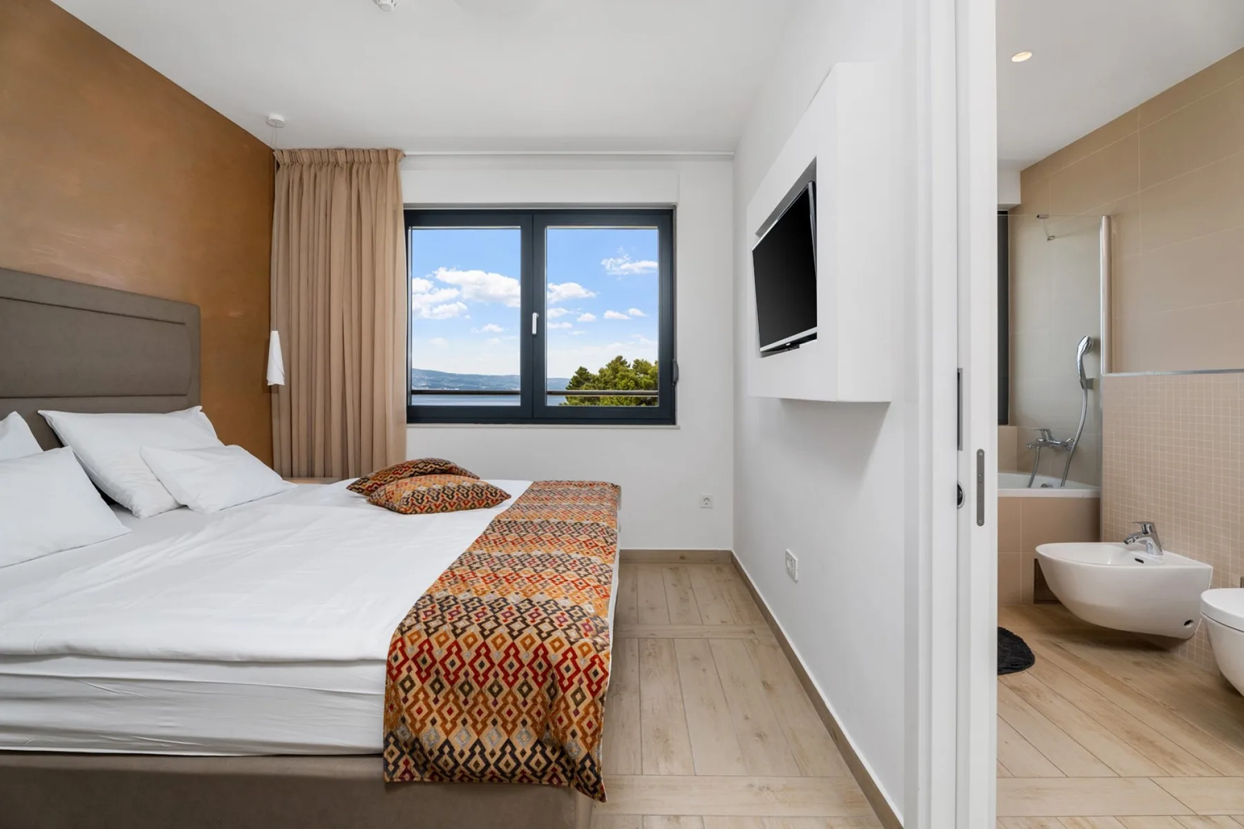 A bedroom with a bed, patterned blanket, and window overlooking a green landscape.