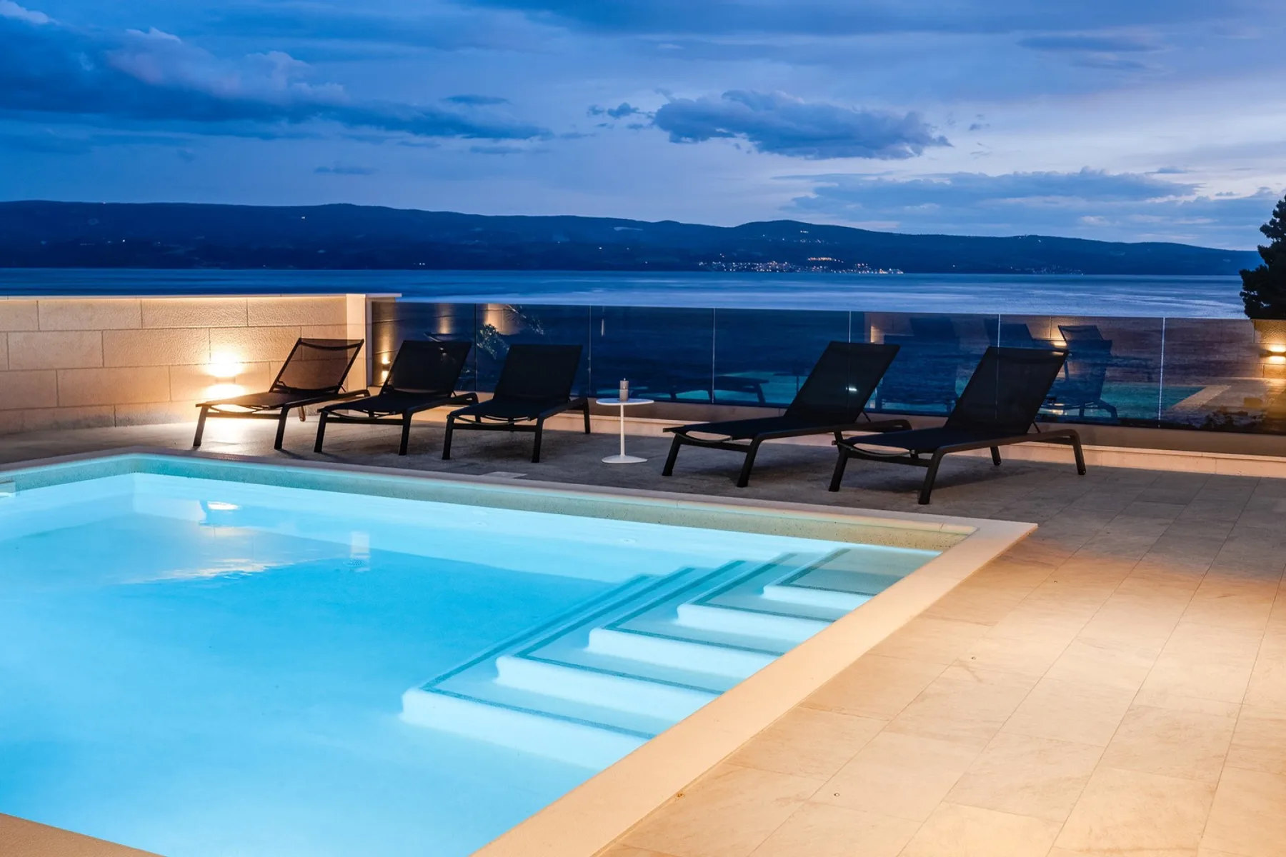 An outdoor swimming pool beside lounge seating, overlooking the water.