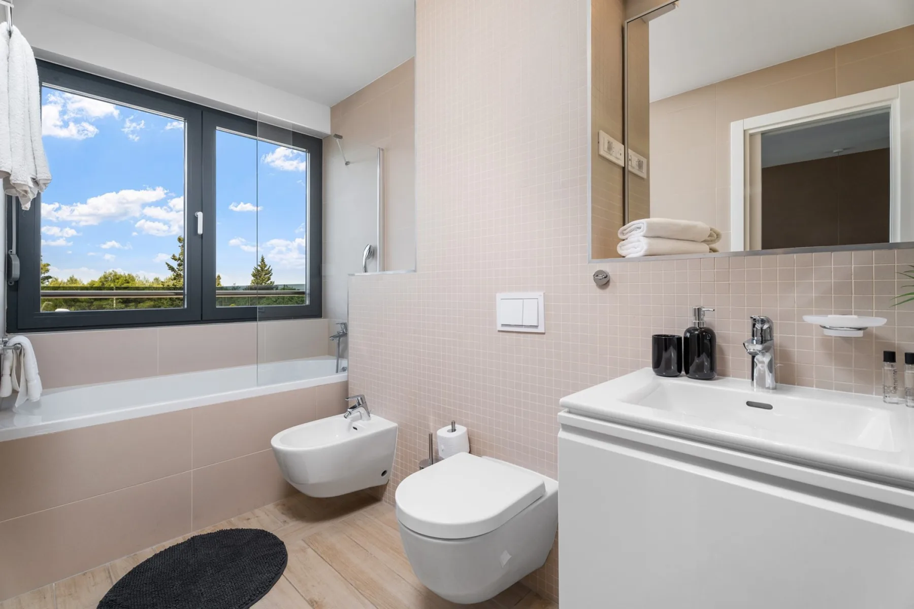 A bathroom with a bathtub, toilet, and sink beneath a large window.