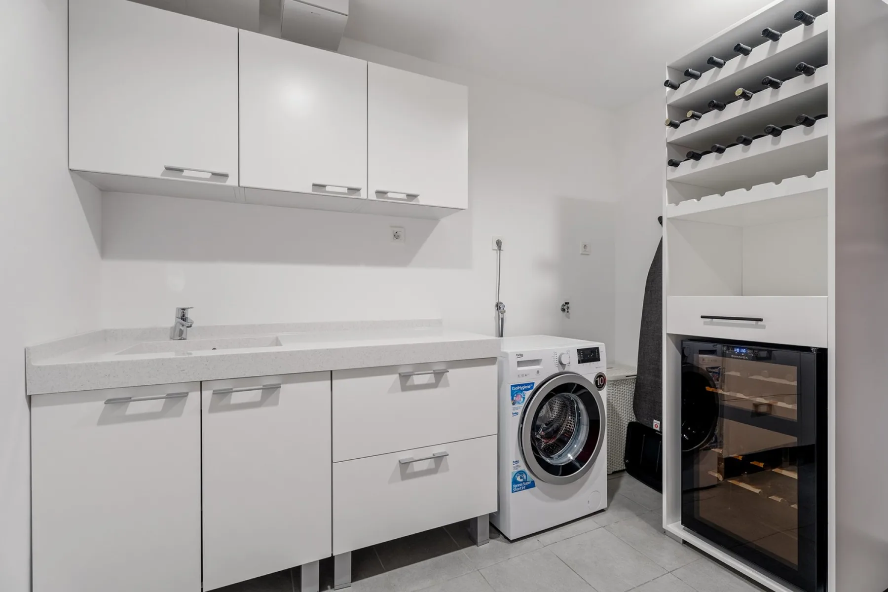 A bright utility room with white cabinets, a washing machine, and a built-in oven.