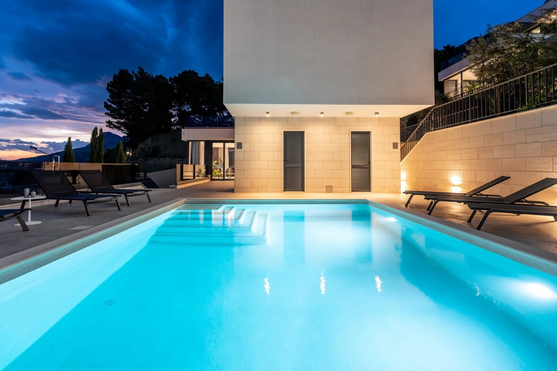 An illuminated outdoor pool beside a modern building at dusk.