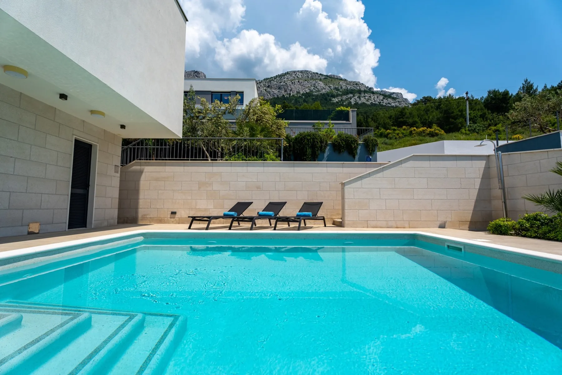 A swimming pool beside a modern building, with loungers along the far edge.
