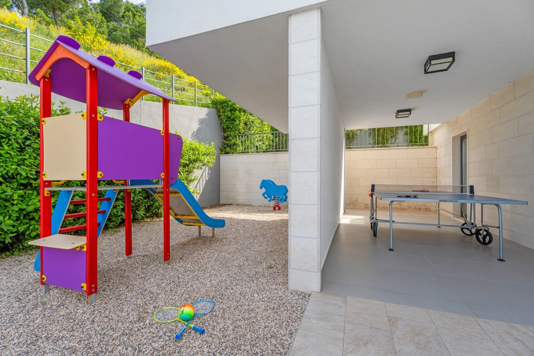 A covered recreation area with a playground slide and a table tennis table.
