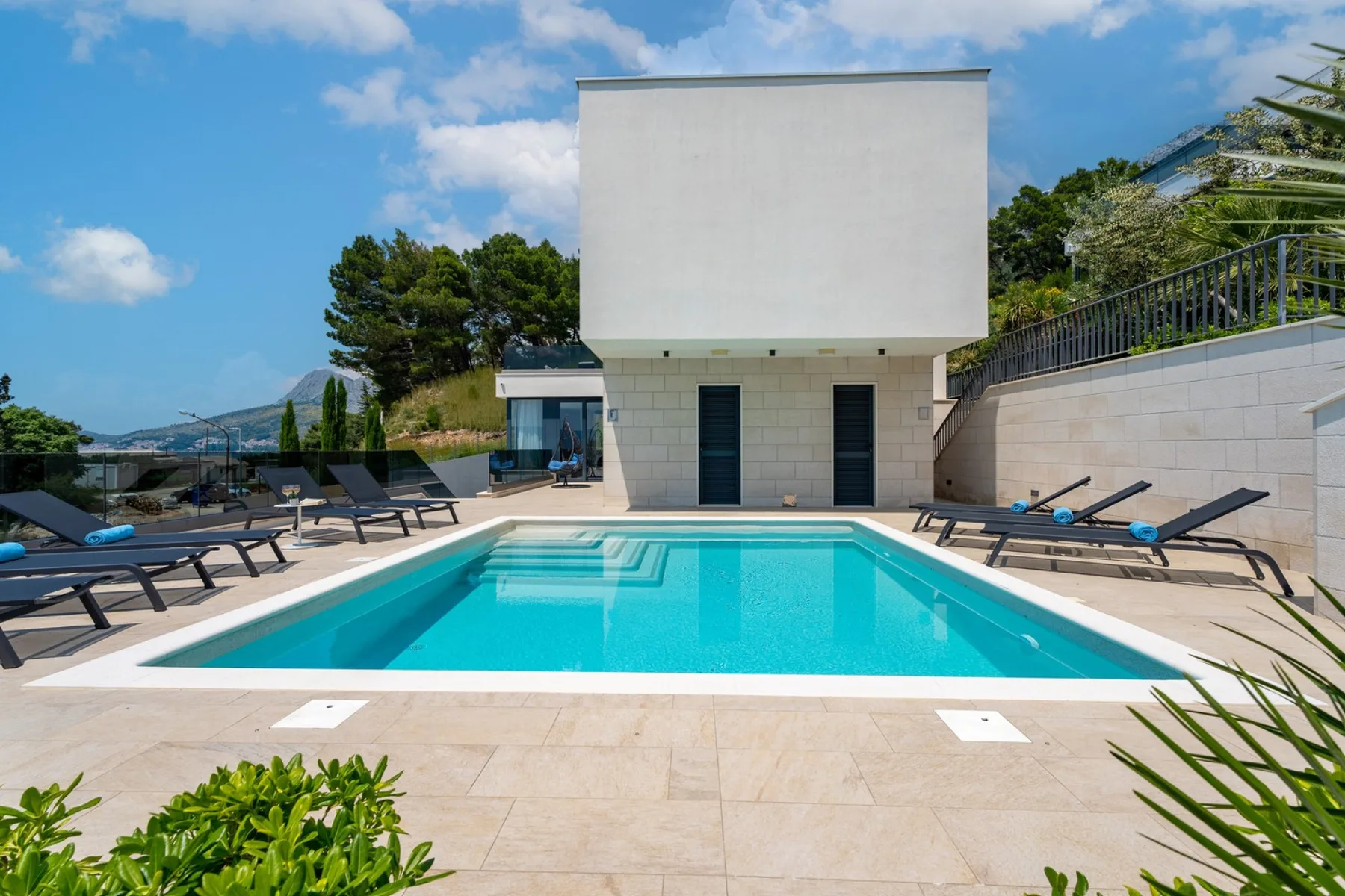 An outdoor swimming pool sits beside a modern building and paved terrace.