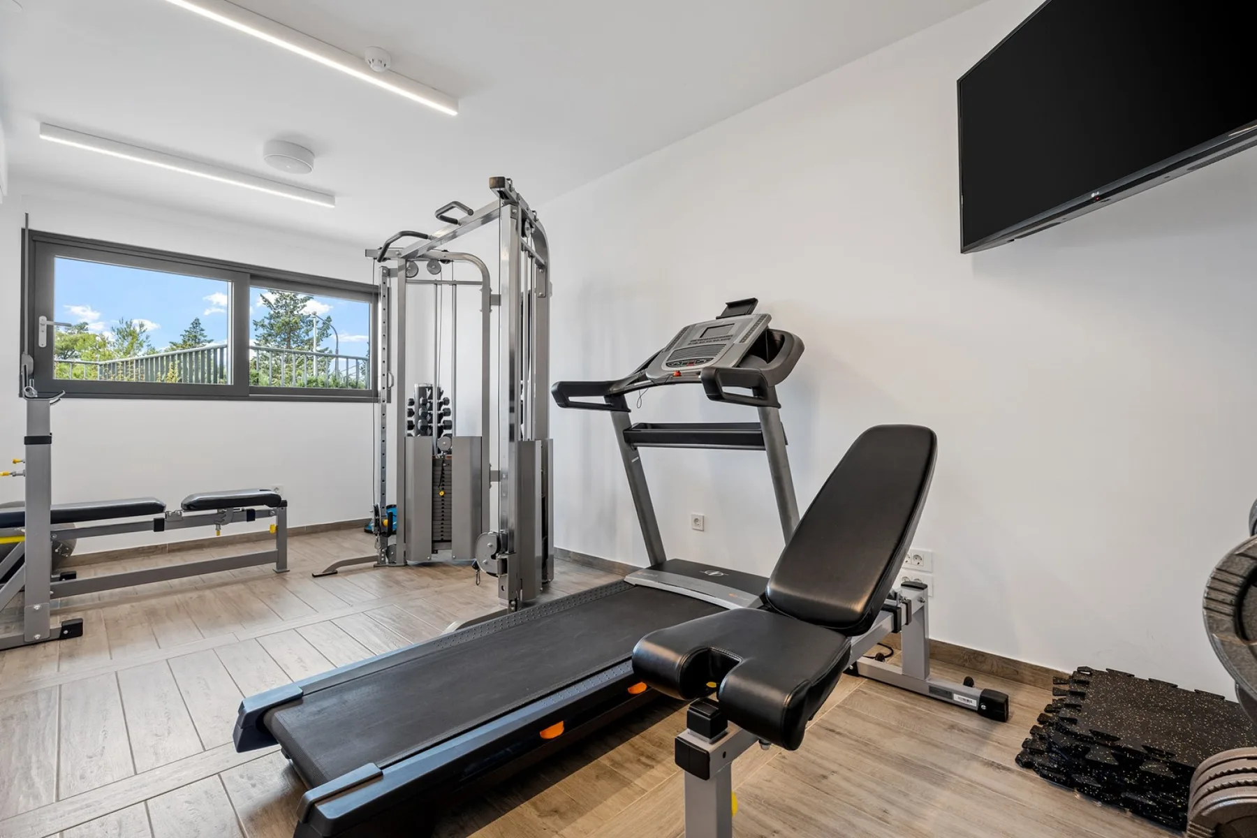 A home gym with exercise equipment and a treadmill beside a large window.